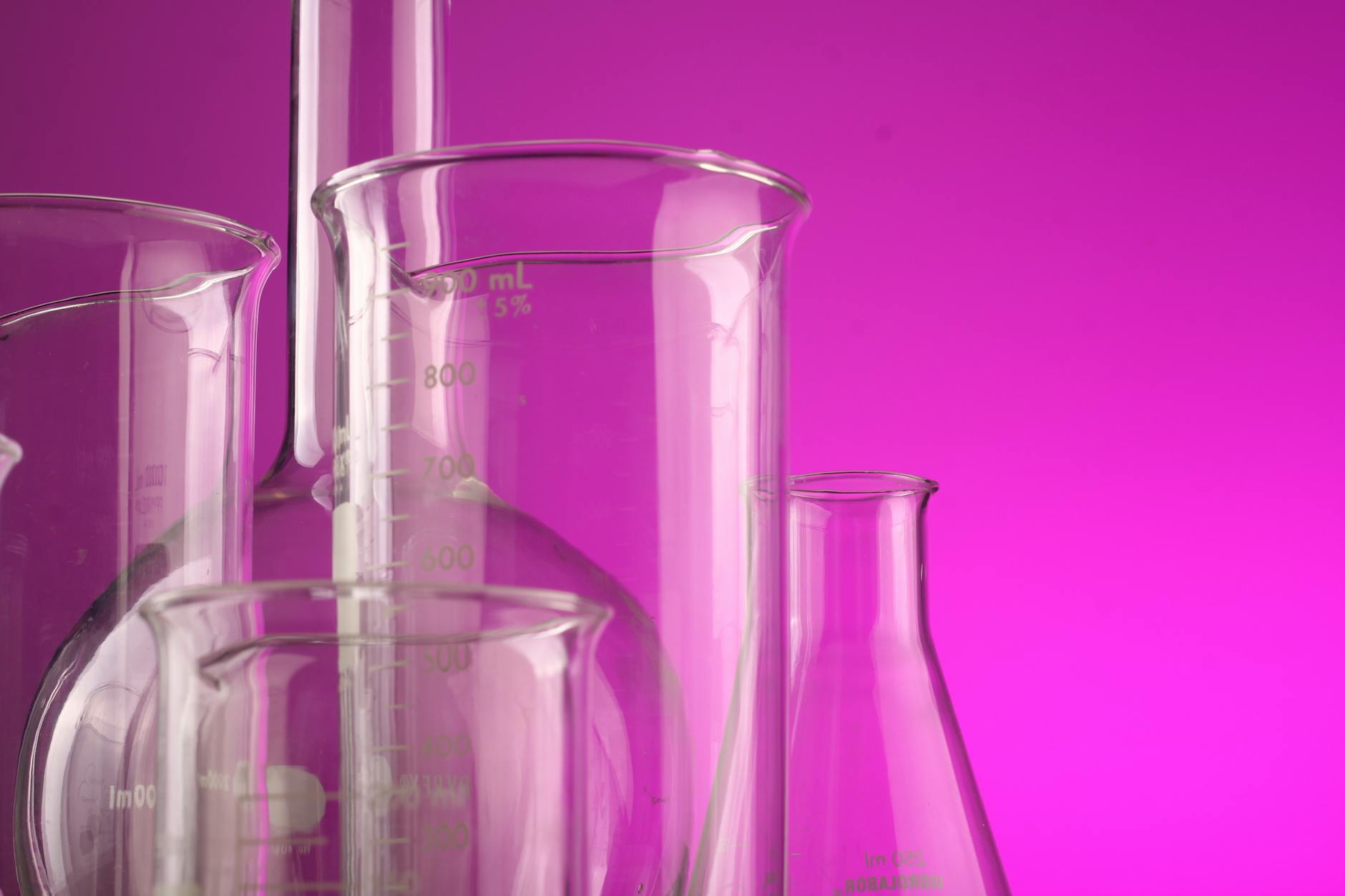 Clear glass laboratory flasks with volume measurements against a vibrant purple backdrop, ideal for science themes.