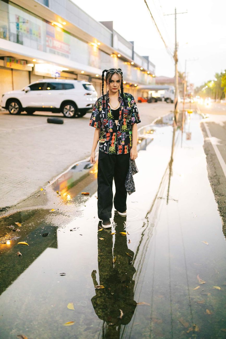 A fashionable woman walks along a city street with a vivid reflection in a puddle, showcasing urban style.