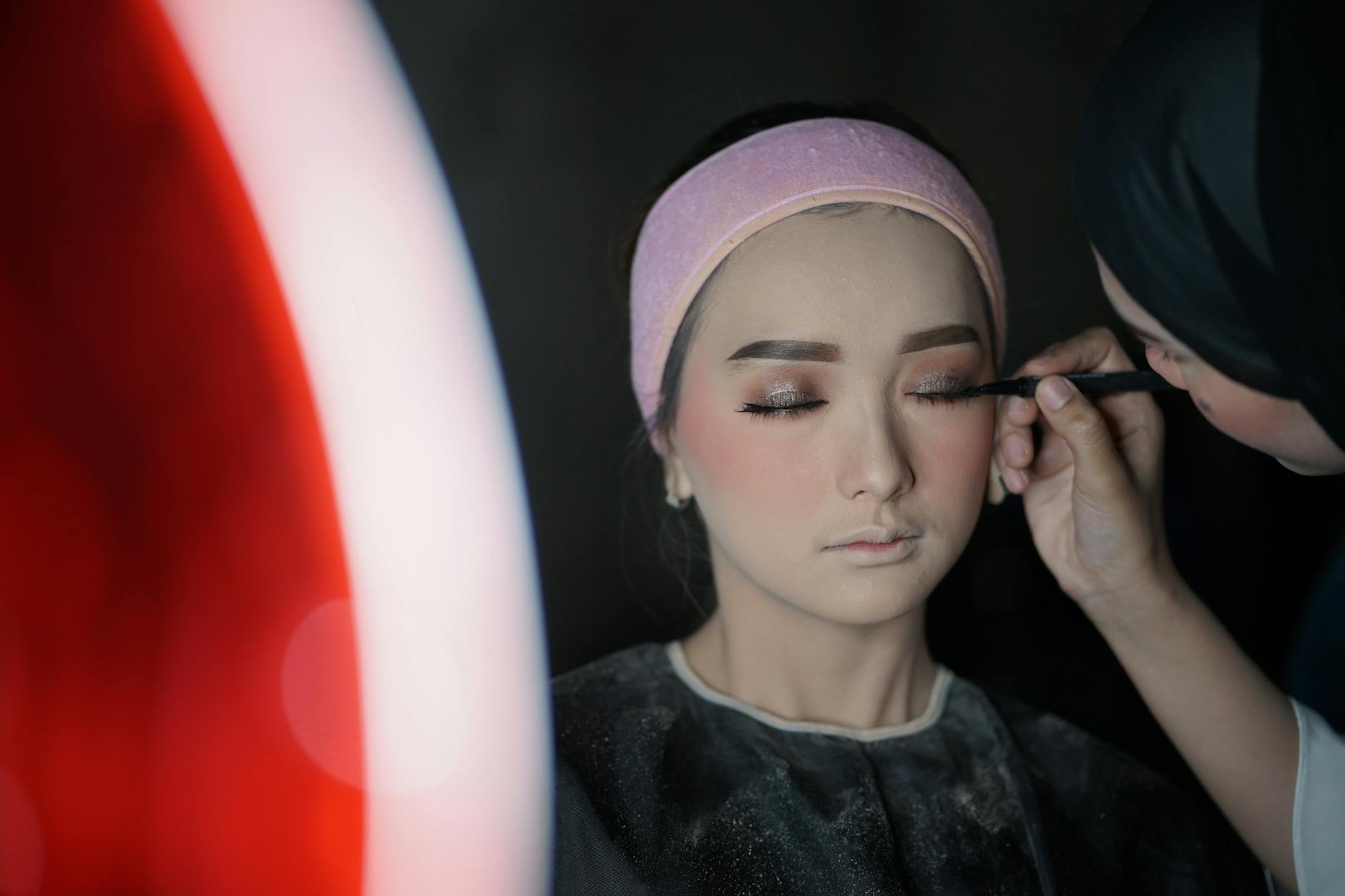 A close-up portrait of a woman receiving professional makeup application indoors.