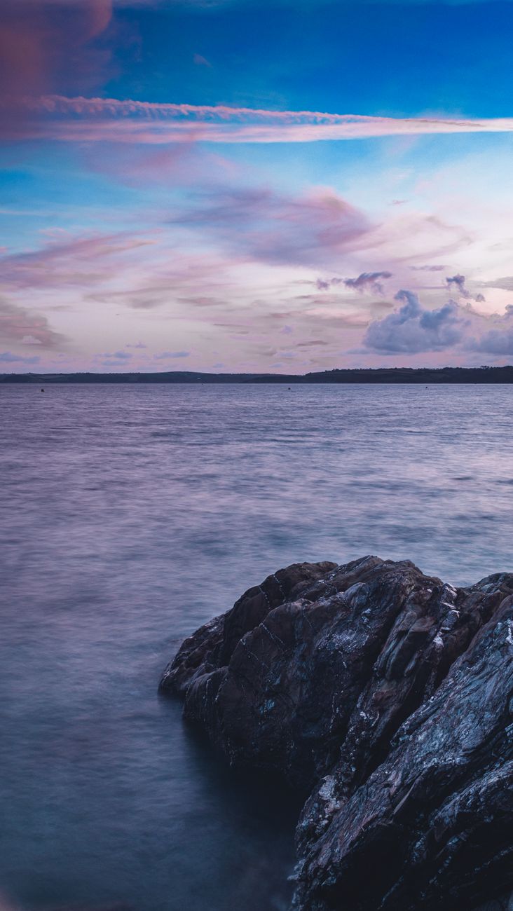 Serene ocean and rocky shore at dusk in Falmouth, England, with a colorful sky.