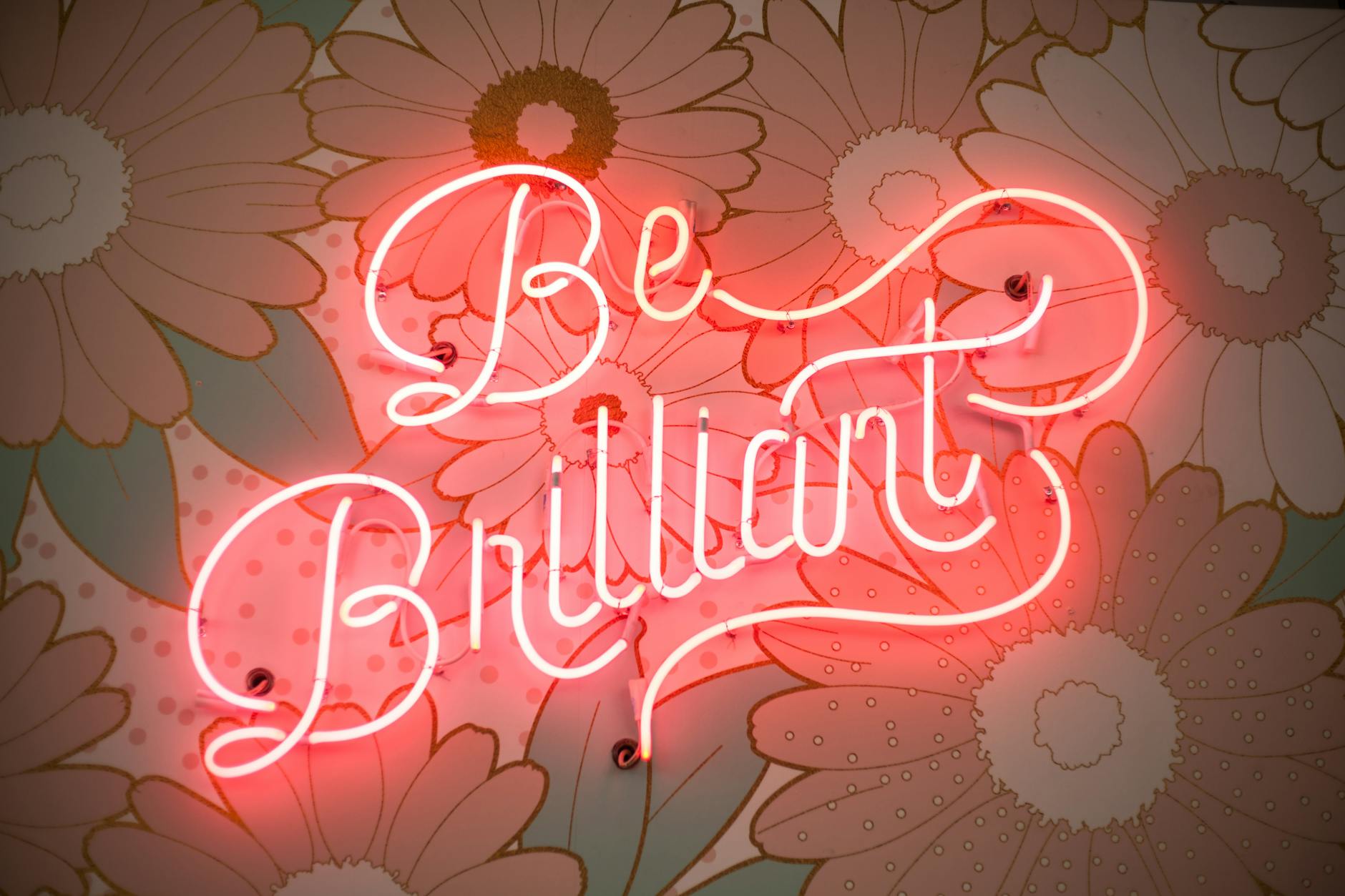 A glowing neon sign reading 'Be Brilliant' against a floral backdrop creates a vibrant and motivational atmosphere.
