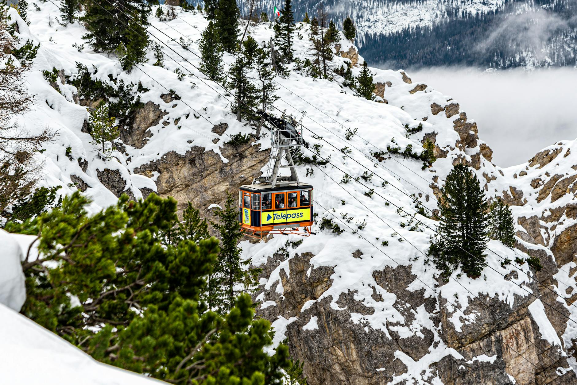 Cable car navigating snowy cliffs in Cortina d'Ampezzo, Italy during winter.