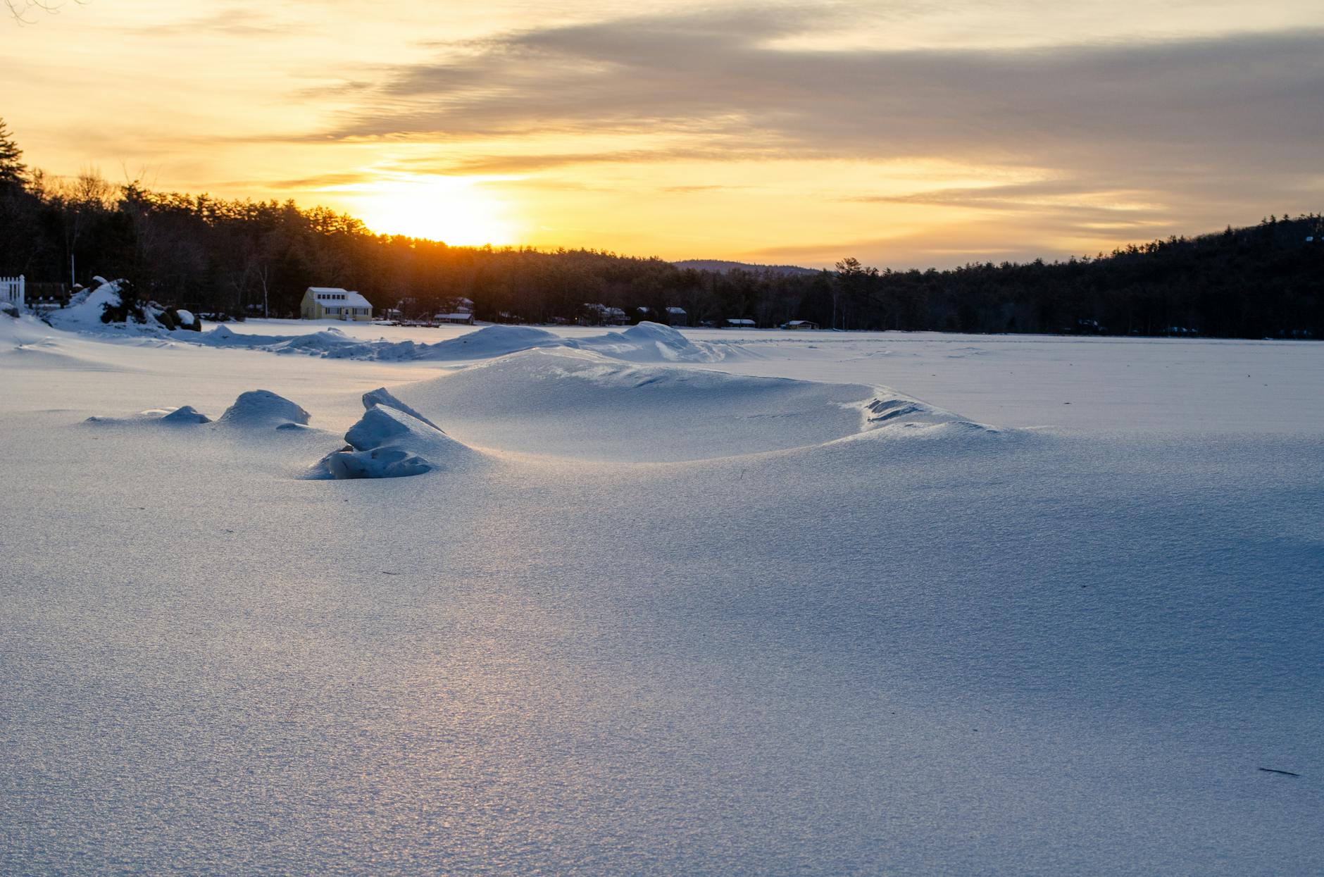Tranquil winter sunset over a snowy frozen lake, surrounded by trees.