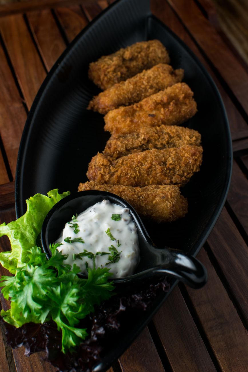 Close-up of crispy fried croquettes served with dip and fresh greens on a black plate.