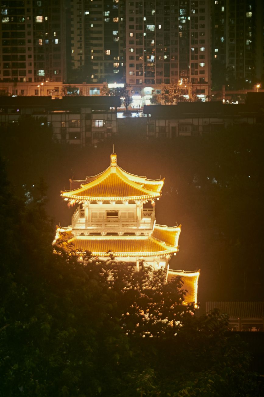A beautifully lit temple stands out against an urban backdrop at night.
