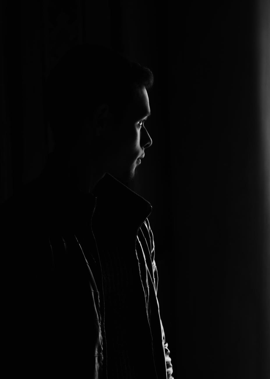 Monochrome portrait of a man in silhouette looking out a window.