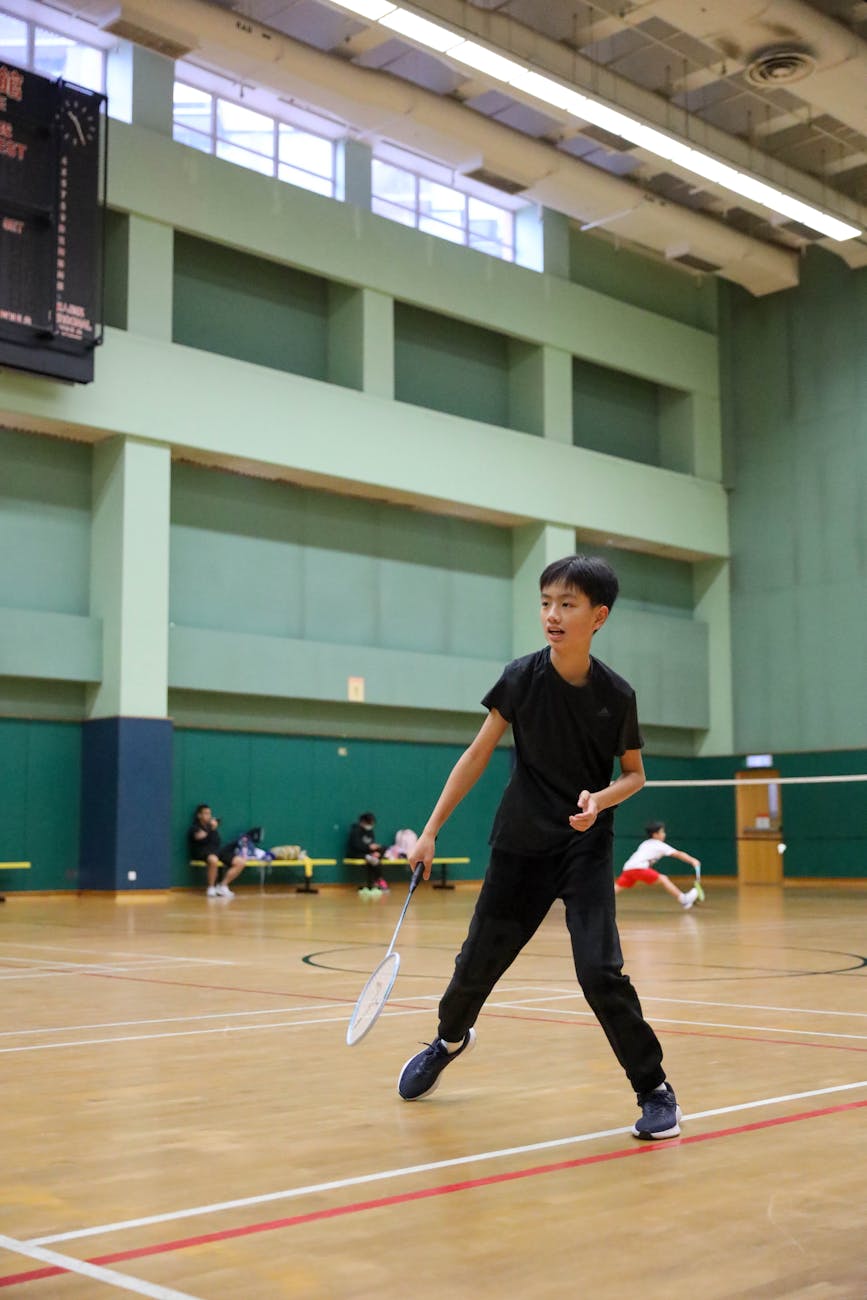 Young boy focused on playing badminton in an indoor gym setting.