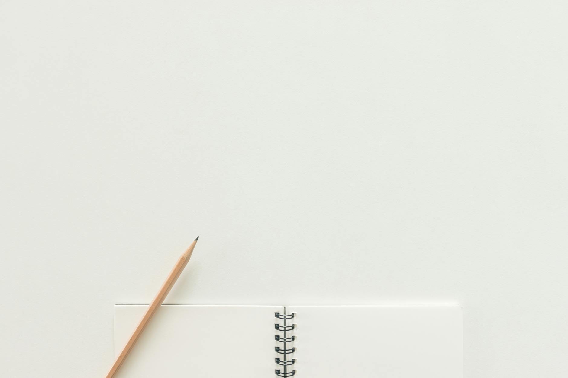 A top view of a spiral notebook with pencil on a neutral light background, ideal for creative workspaces.