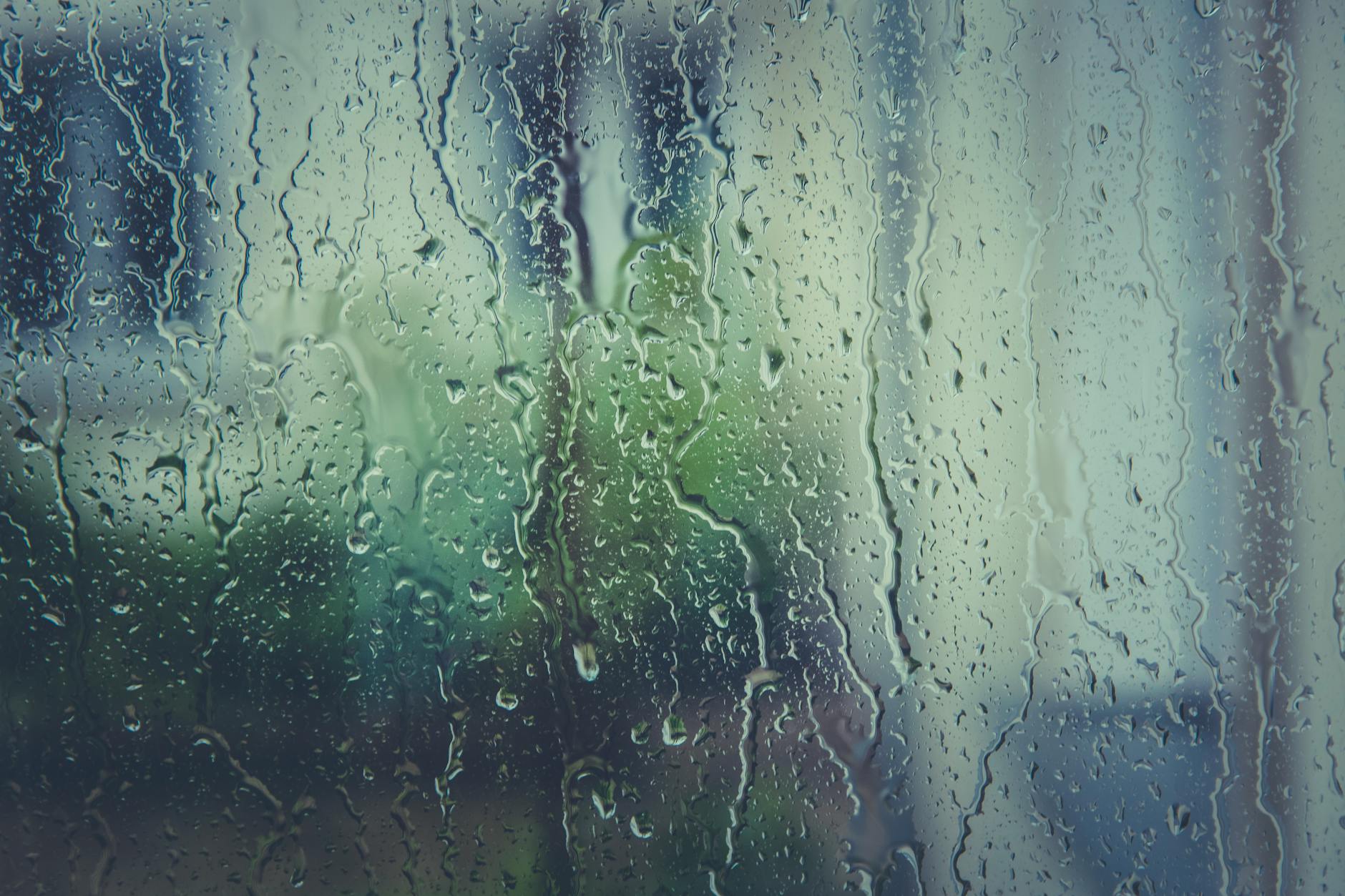 Close-up of raindrops on a window with a blurred natural backdrop, evoking a rainy day mood.