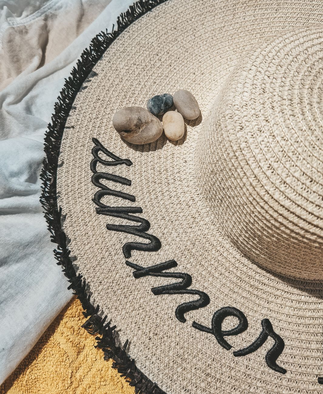 Stylish straw hat with 'summer' text adorned with pebbles, perfect for beach days.