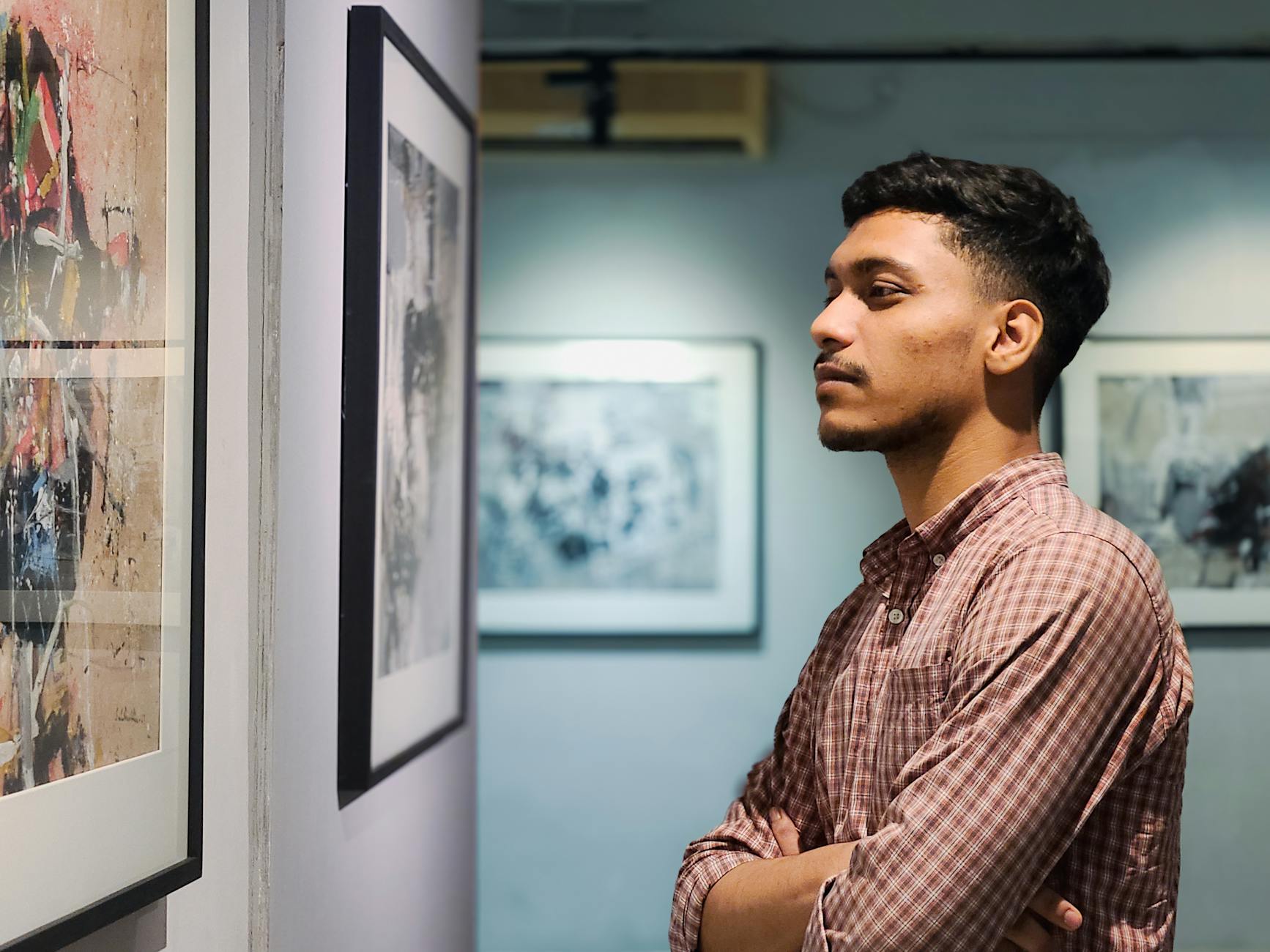 Young man admiring artwork in a contemporary art gallery with framed pictures on the wall.