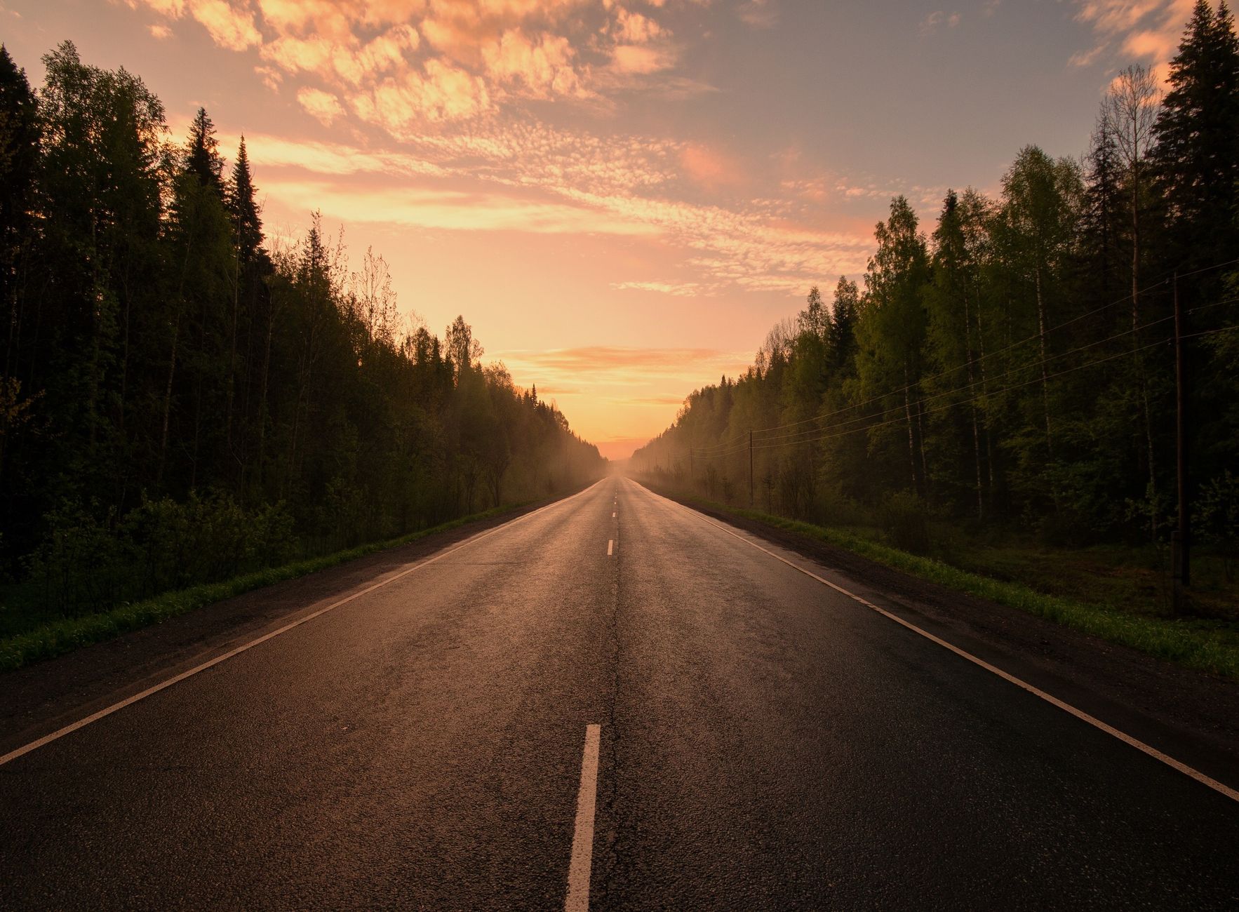 A picturesque highway surrounded by trees under a stunning sunset sky.
