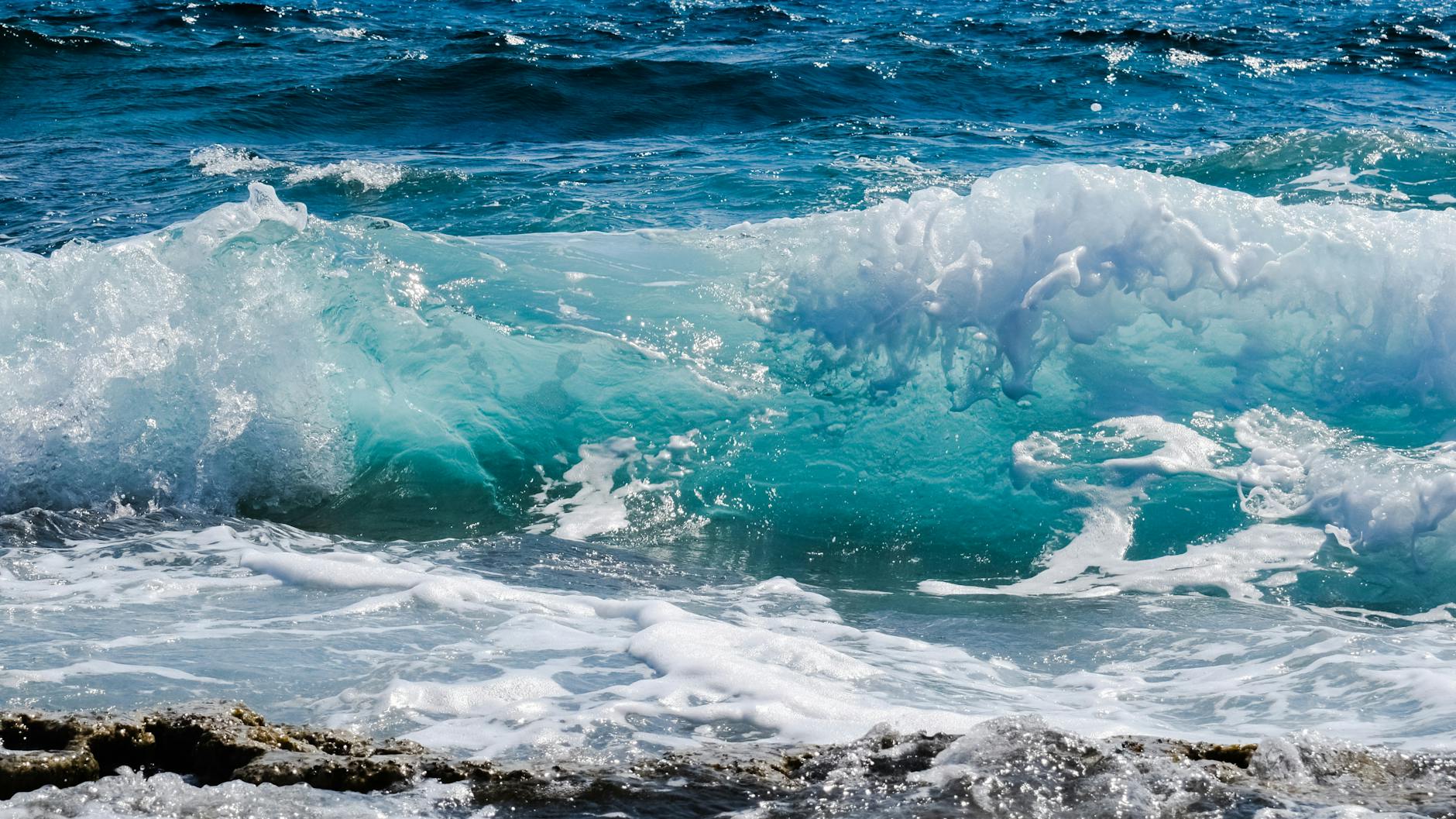 Dynamic ocean waves splashing against rocky shore, capturing sea foam and deep blue hues.