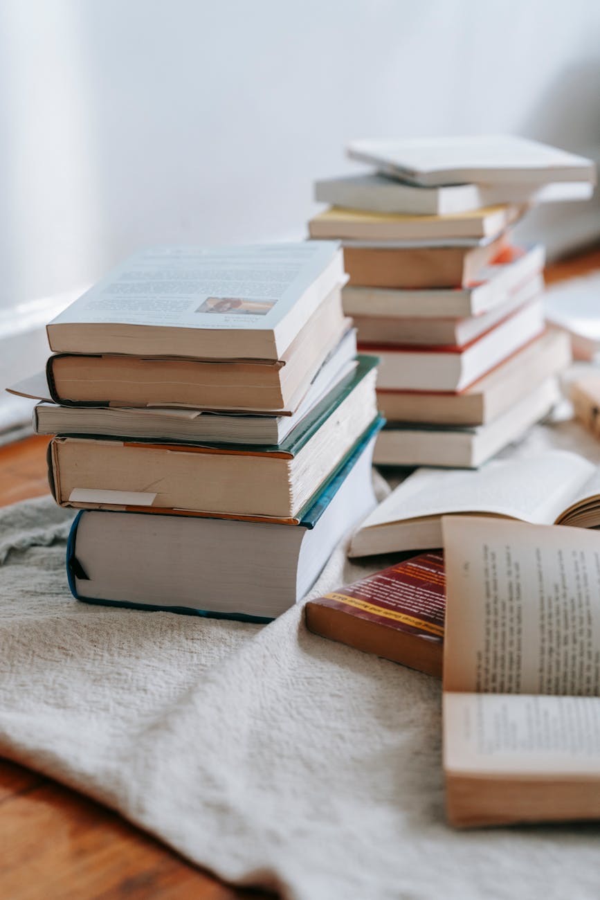 Stack of opened and closed books placed on white soft fabric on floor near wall in light room at home