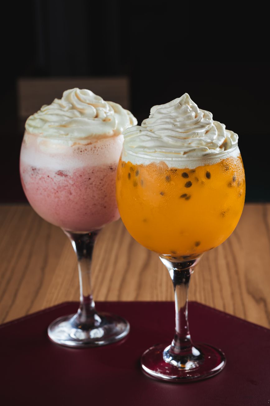 Two elegant cocktails with whipped cream, featuring strawberry and passion fruit flavors.