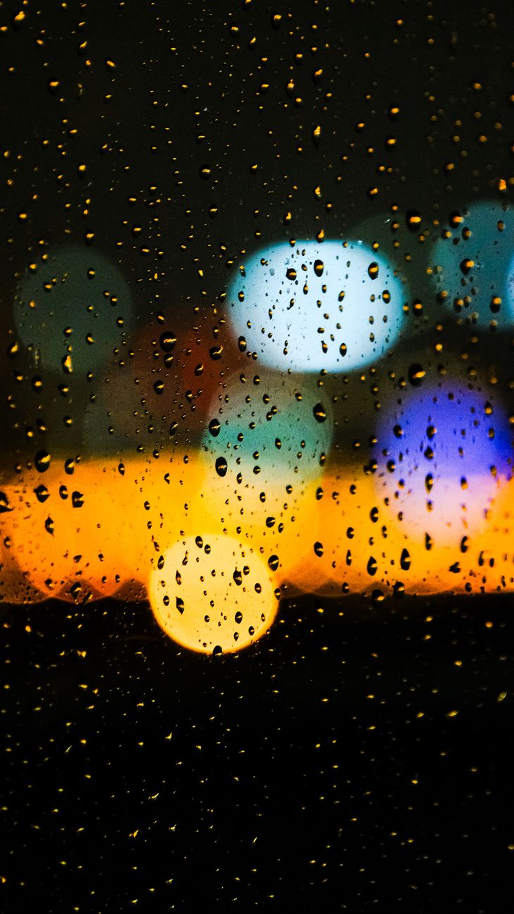 Raindrops on glass with vibrant city lights bokeh creating a moody nighttime scene.