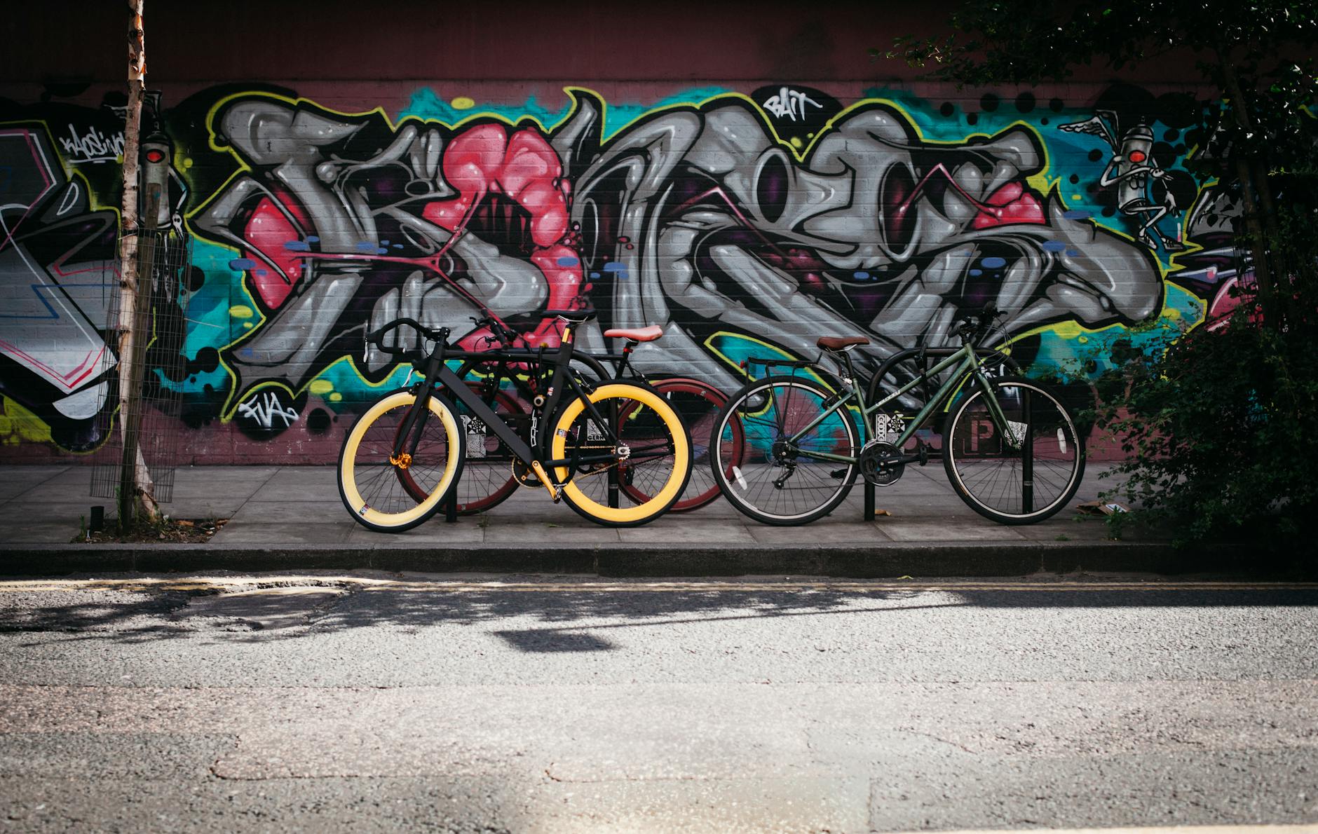 Two bicycles parked against a vibrant graffiti wall on a sunny day, adding urban flair.