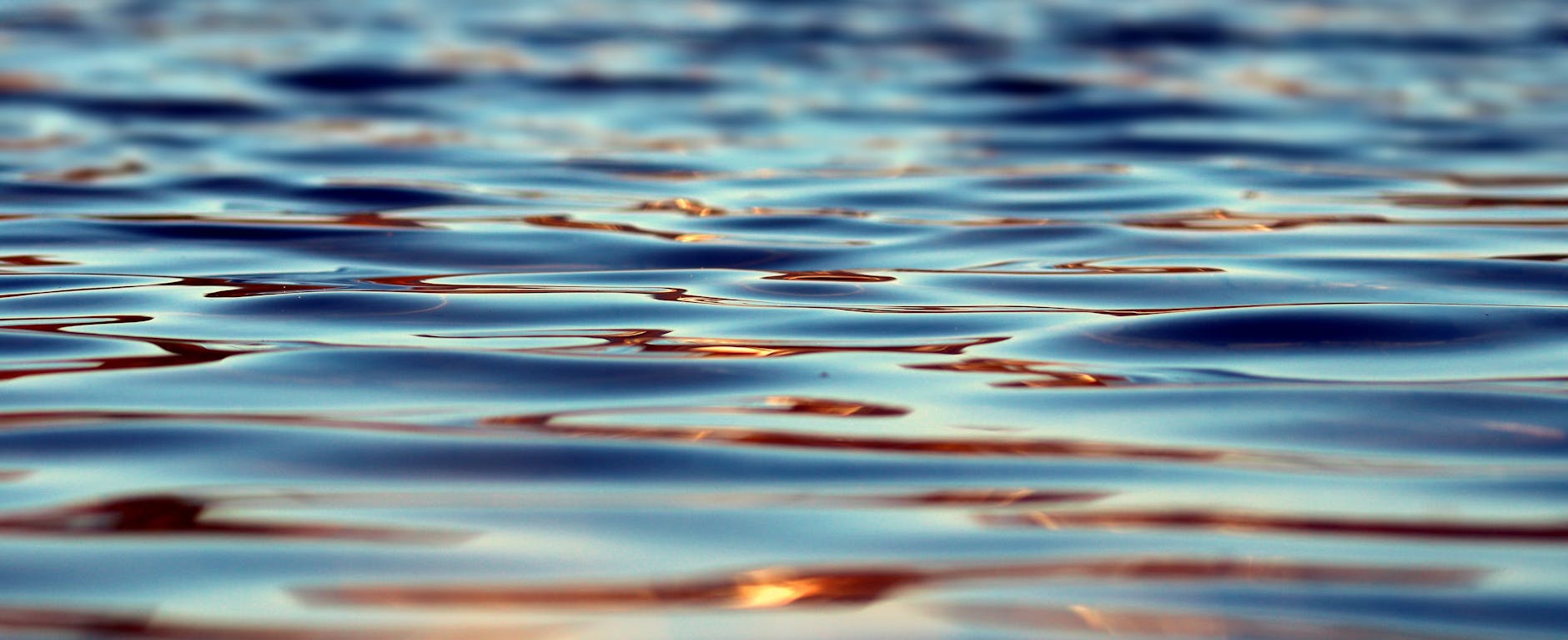 Close-up of serene water surface showcasing gentle ripples and warm reflections in natural light.