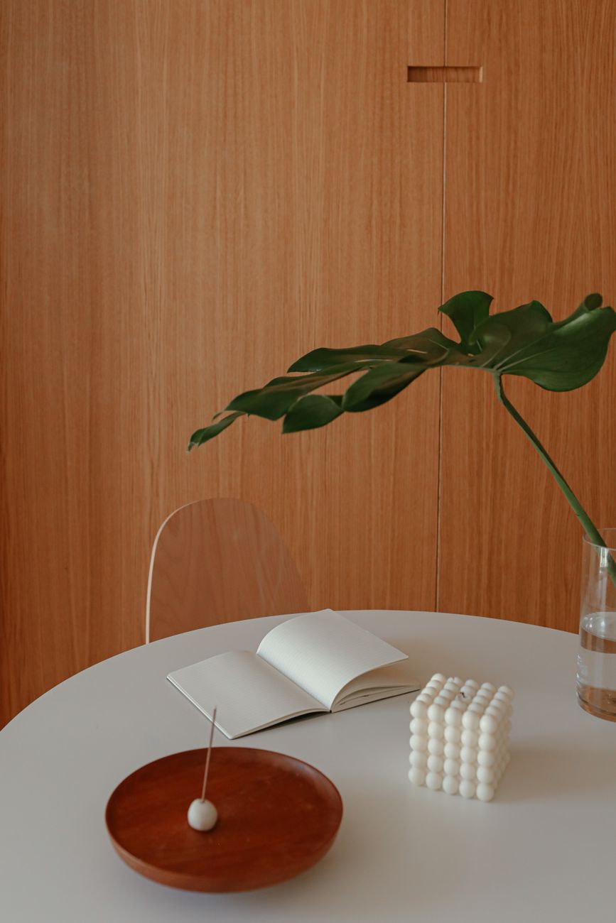 Minimalist table setup with a plant, notebook, and candle for a calm ambiance.