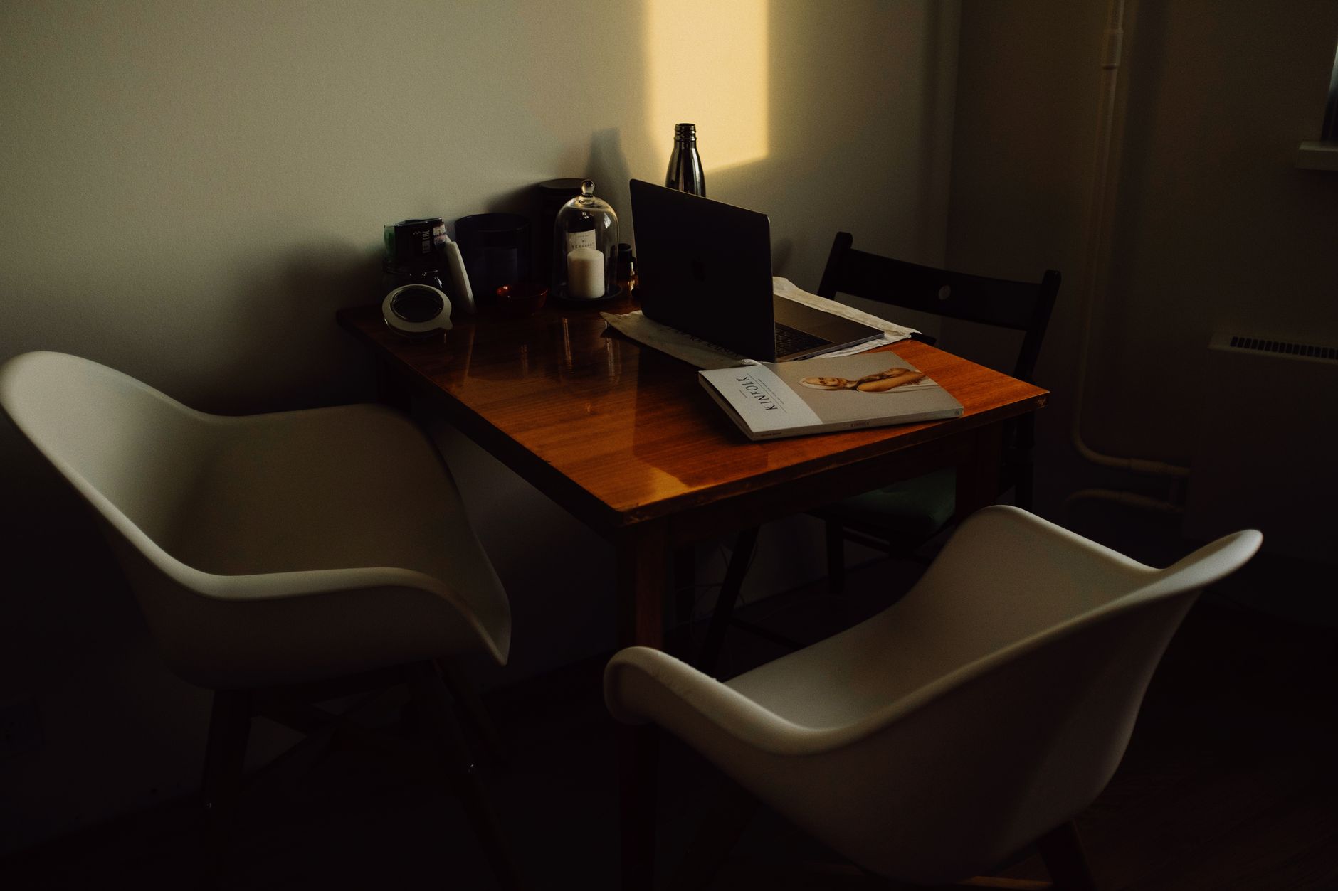 A warm, dark-toned home office with a wooden table and contemporary chairs. Includes a laptop, magazine, and decor.