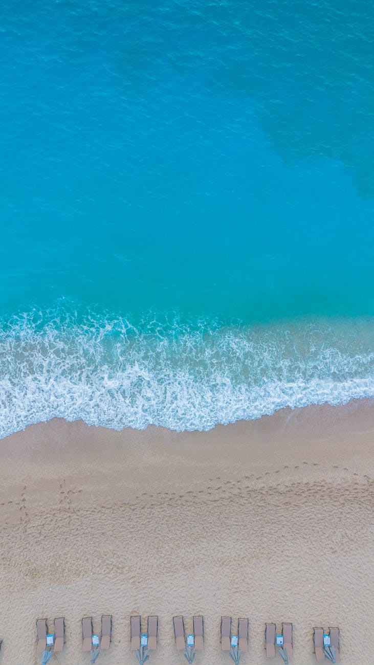 Aerial view of a tranquil beach with turquoise waters and empty lounge chairs, perfect for relaxation.
