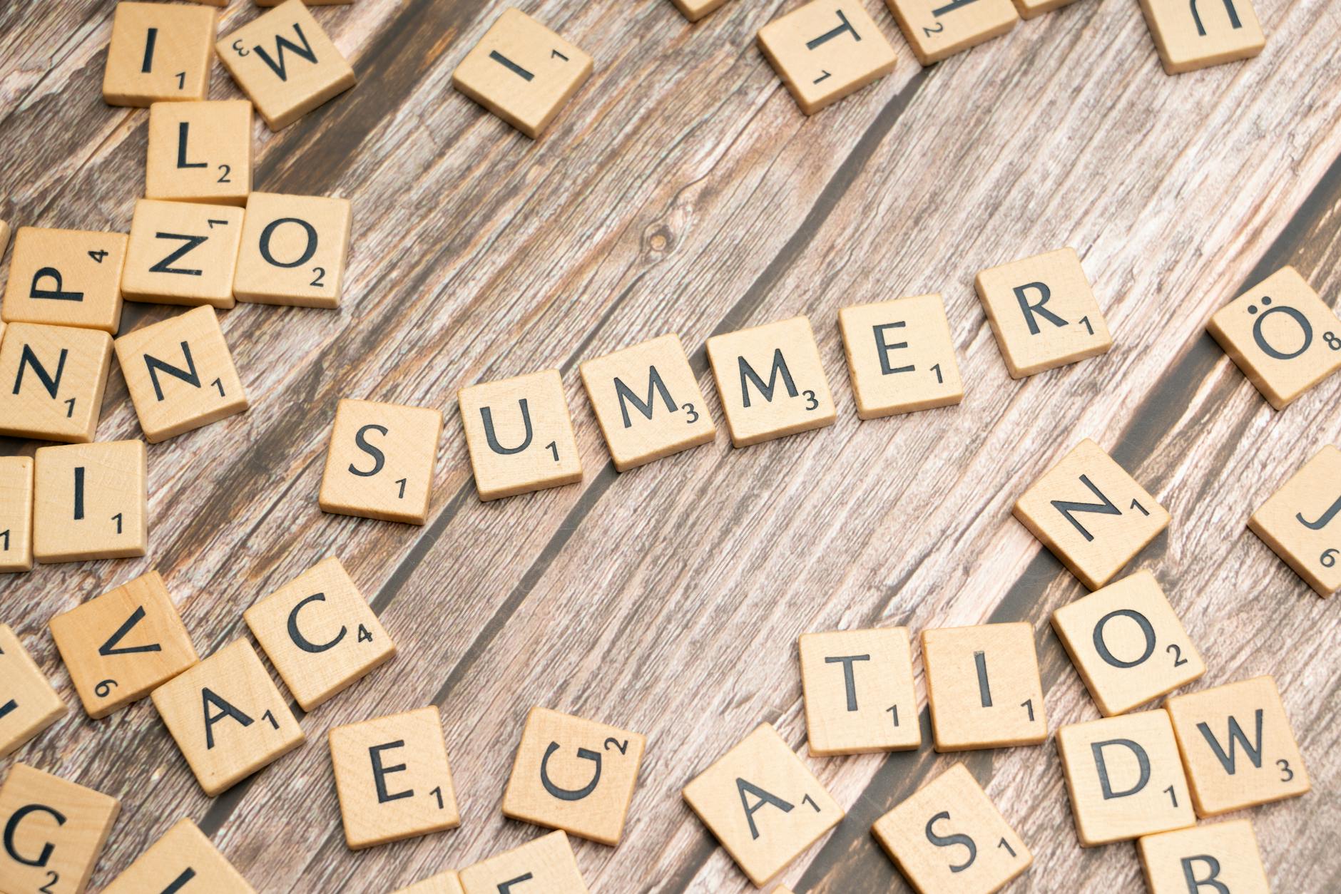 Scrabble tiles spelling 'SUMMER' on a rustic wooden surface, evoking warmth and creativity.