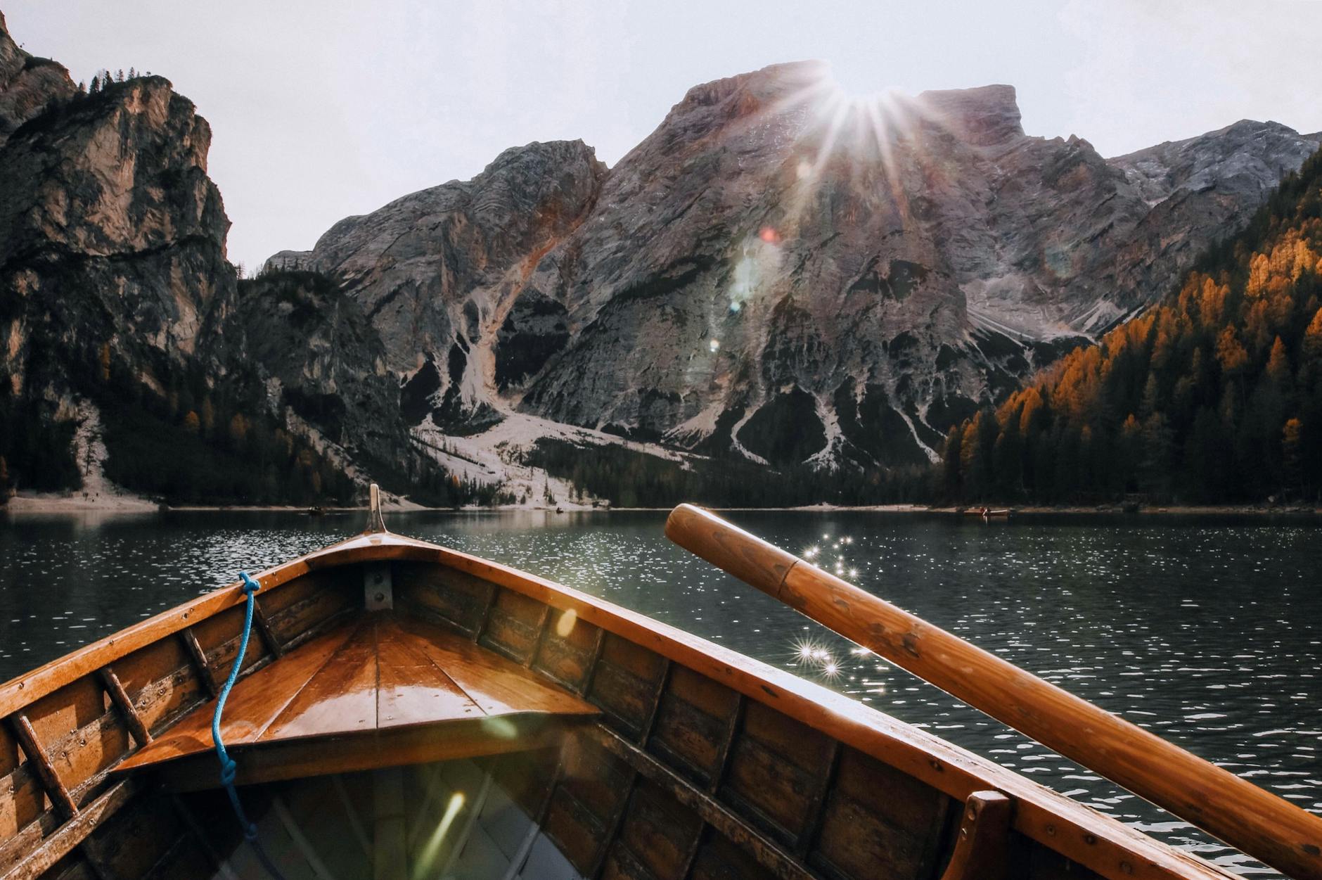 Wooden boat sailing on a serene mountain lake with sunrays illuminating the scenic landscape.