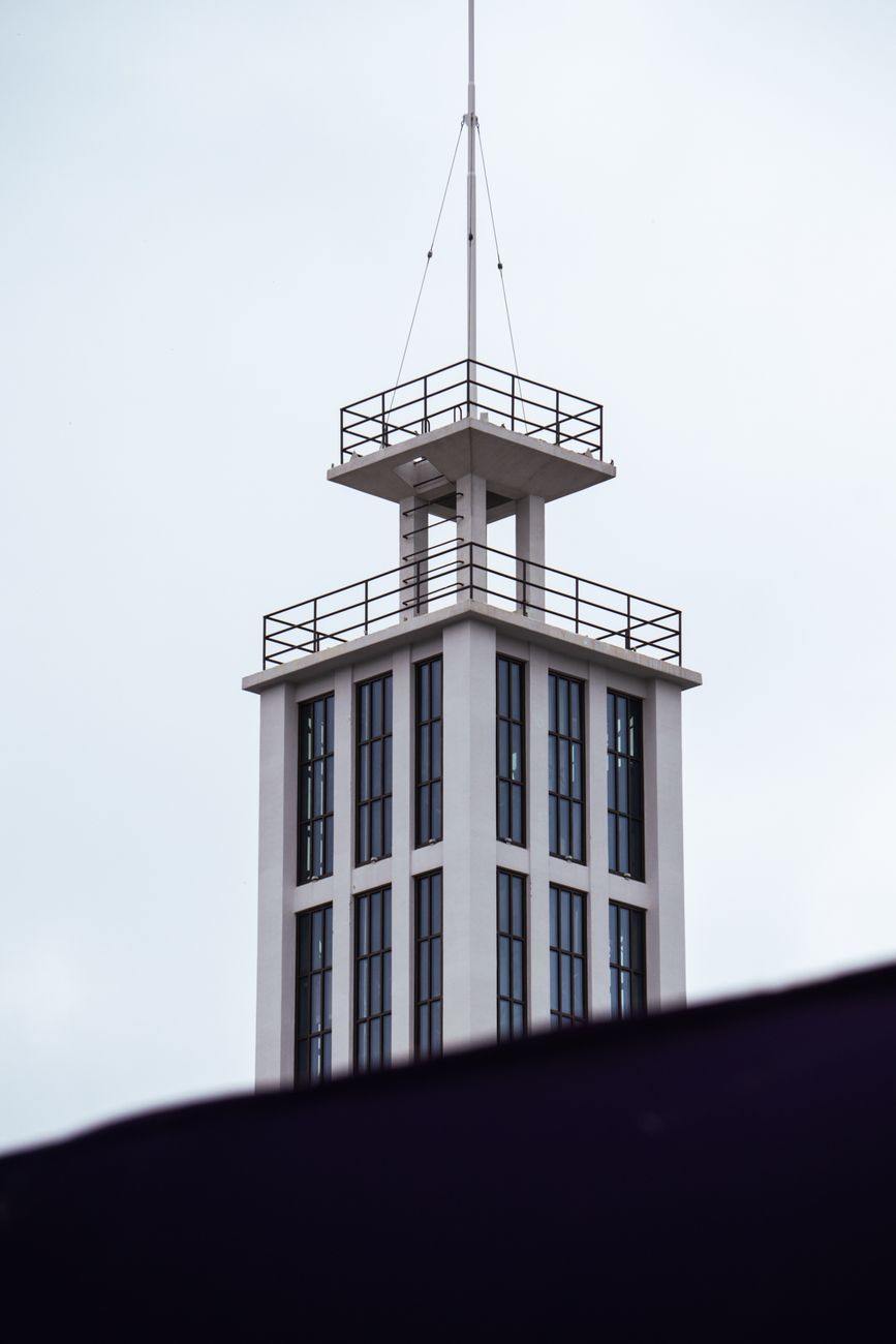 White modern tower with multiple windows and railings against an overcast sky.