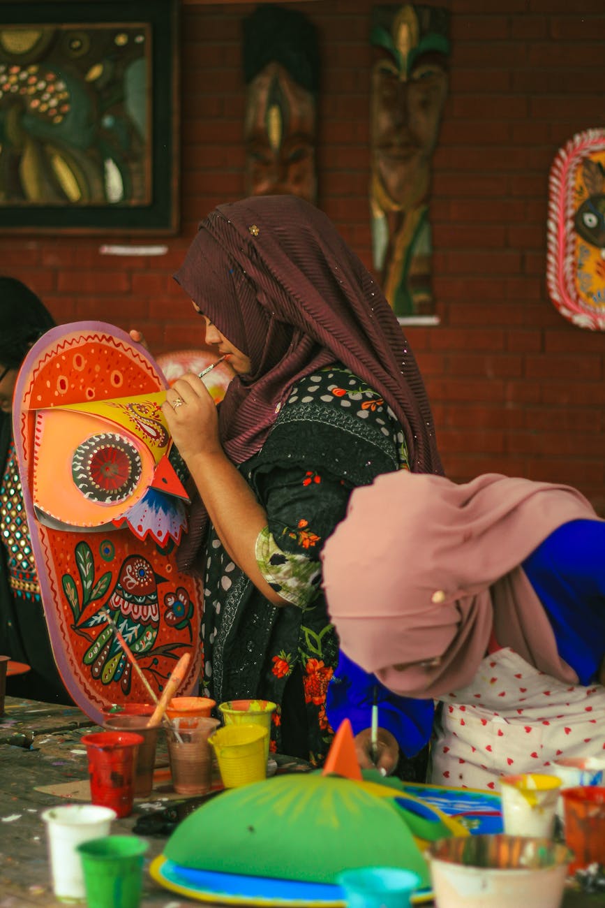 Women artistically painting traditional masks at a fine arts institution in Dhaka, Bangladesh.