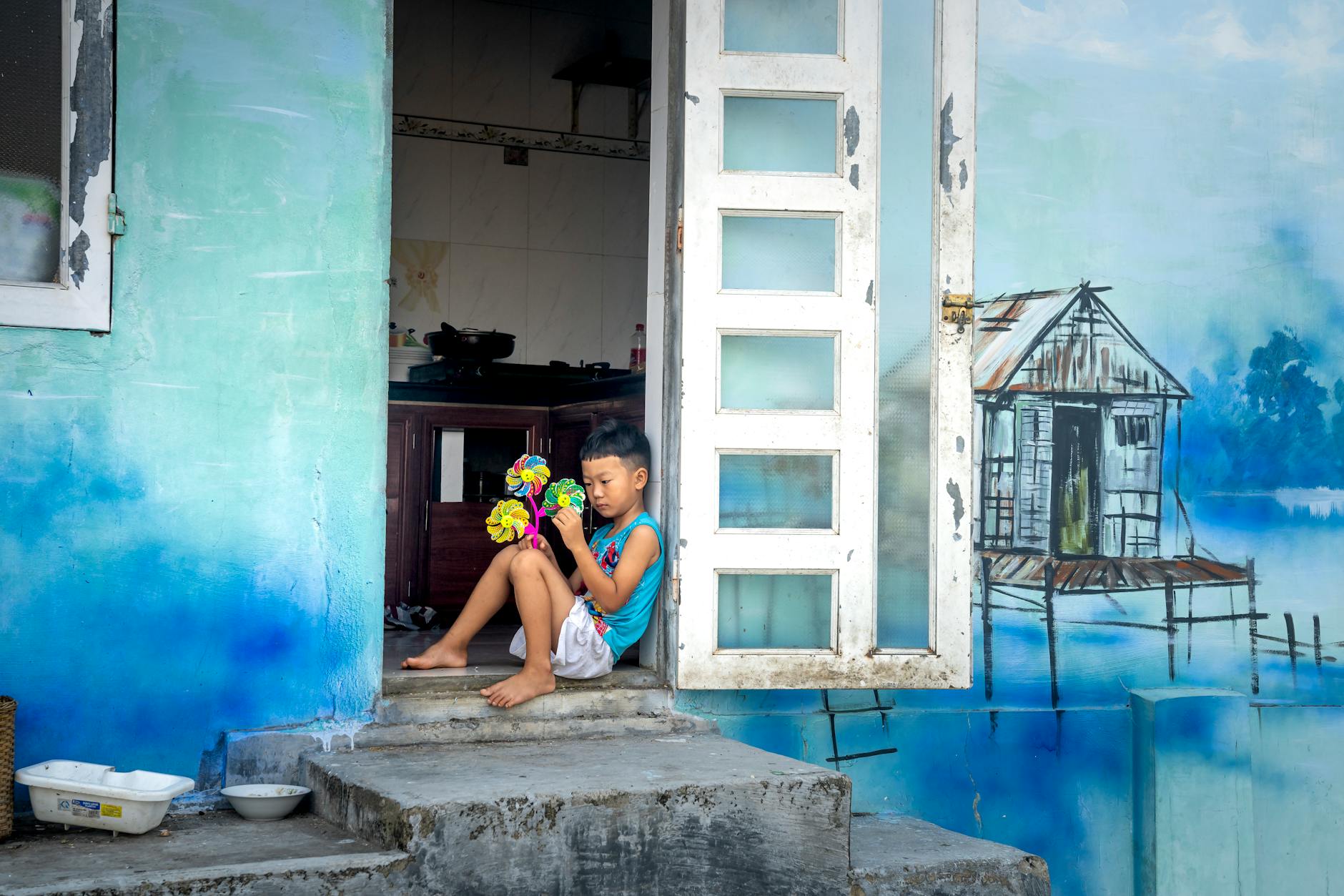 A young boy in a doorway holding a colorful toy, surrounded by street art on the facade.