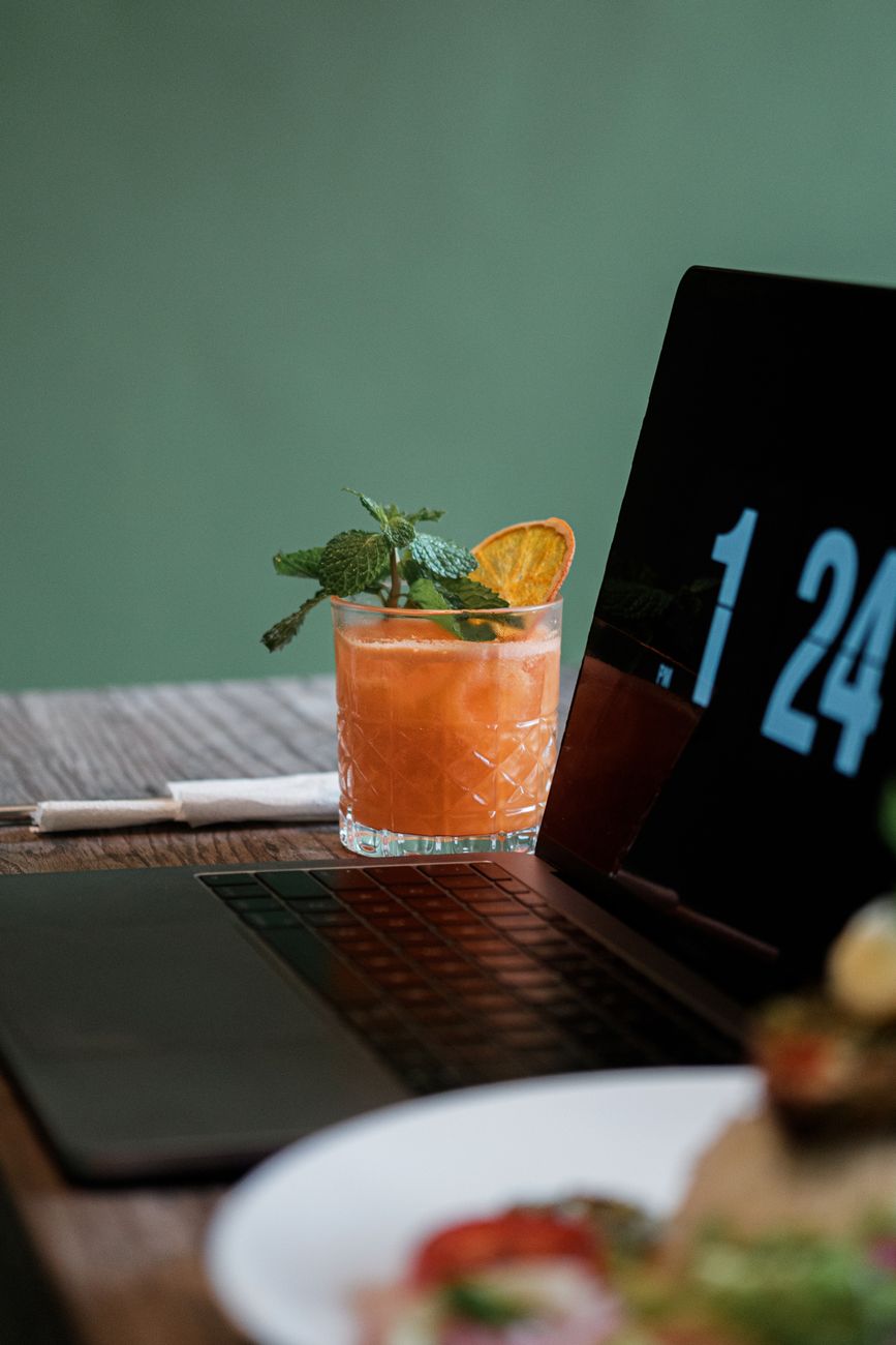 A refreshing citrus cocktail beside a laptop in a stylish workspace setting.