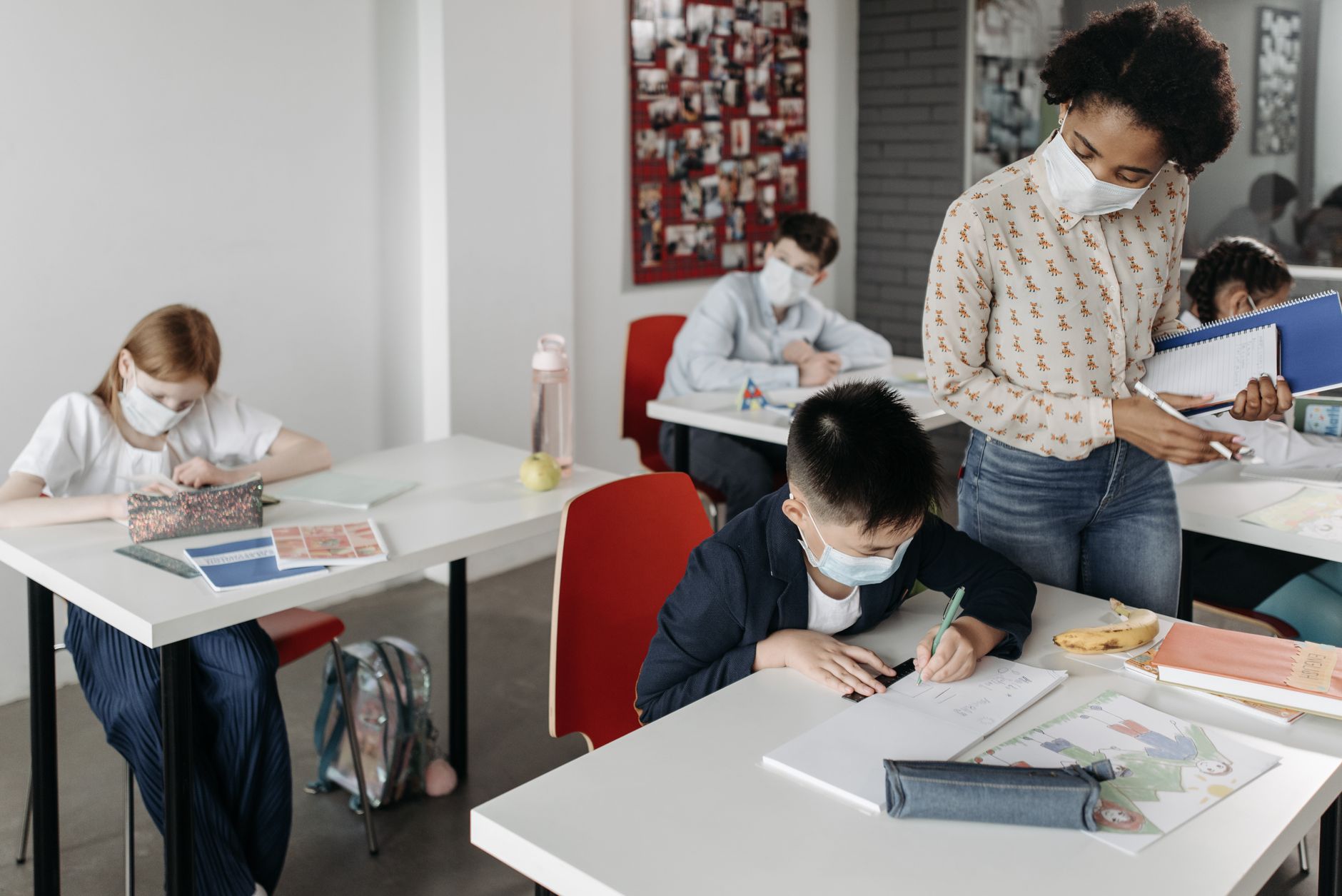 Students and teacher in a classroom setting during pandemic wearing face masks and practicing safety measures.
