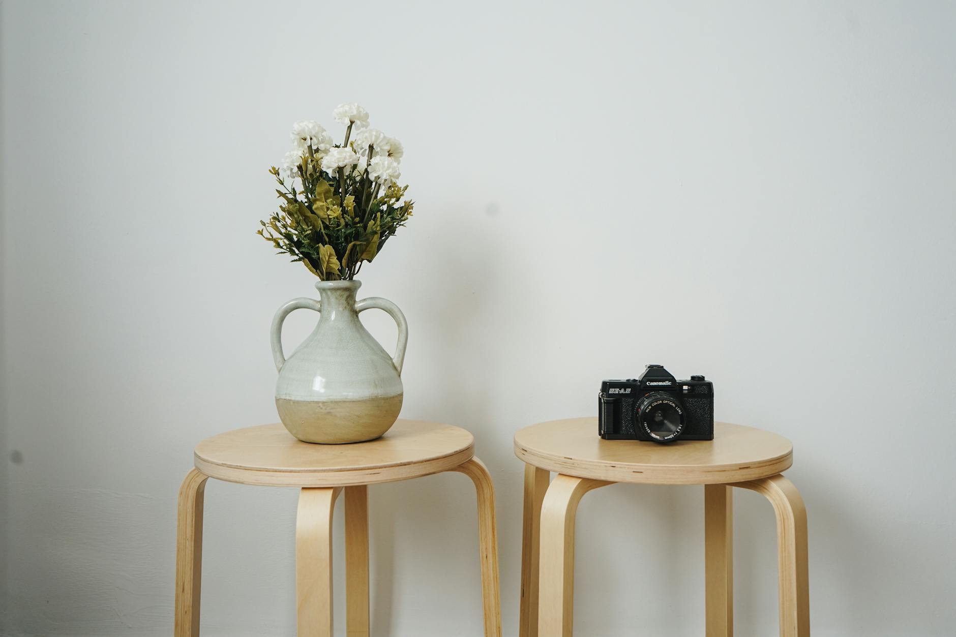 Elegant minimalist setting with a vase of flowers and a camera on wooden stools indoors.