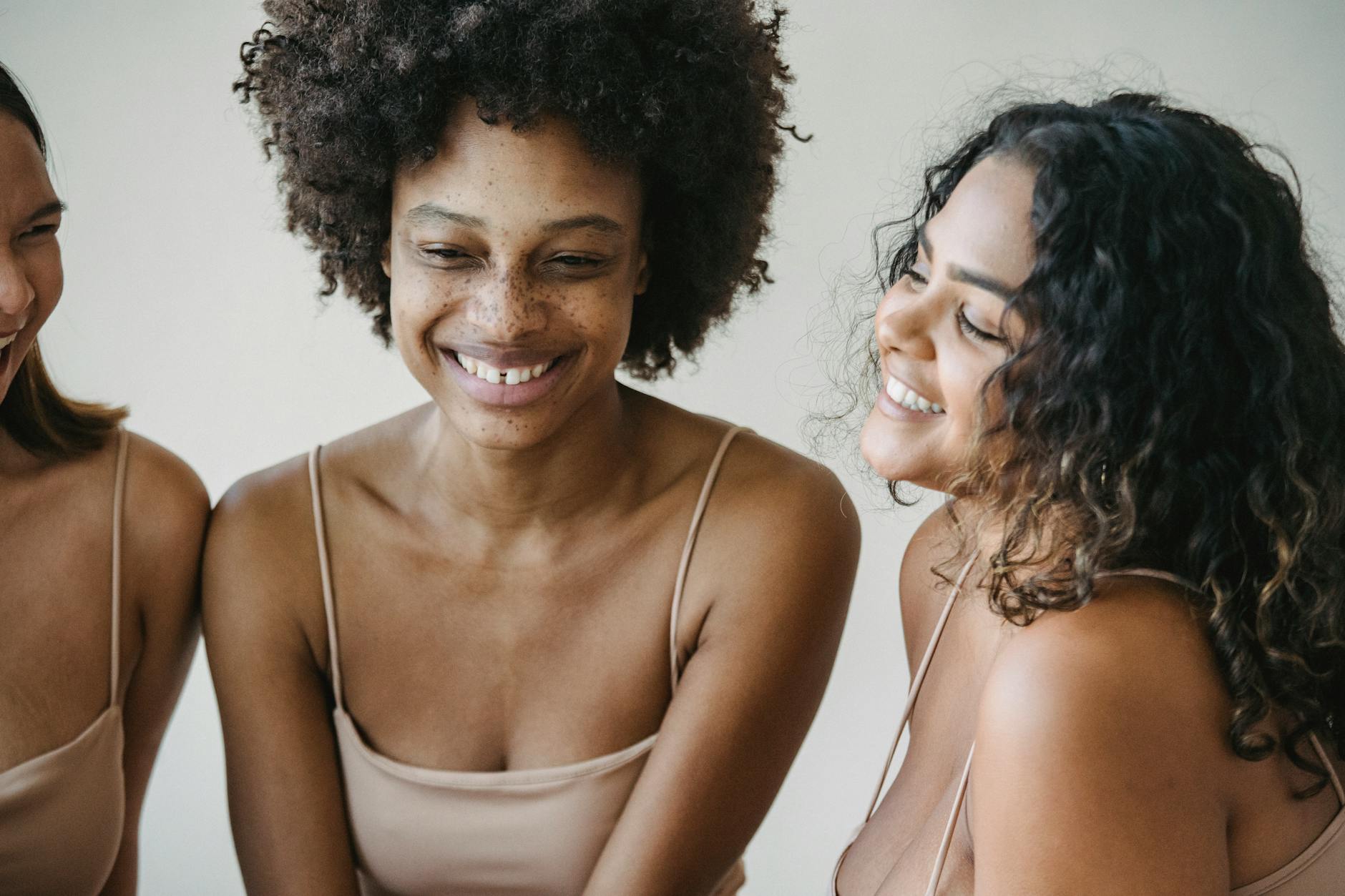 Portrait of three diverse women smiling warmly in a minimalist setting.