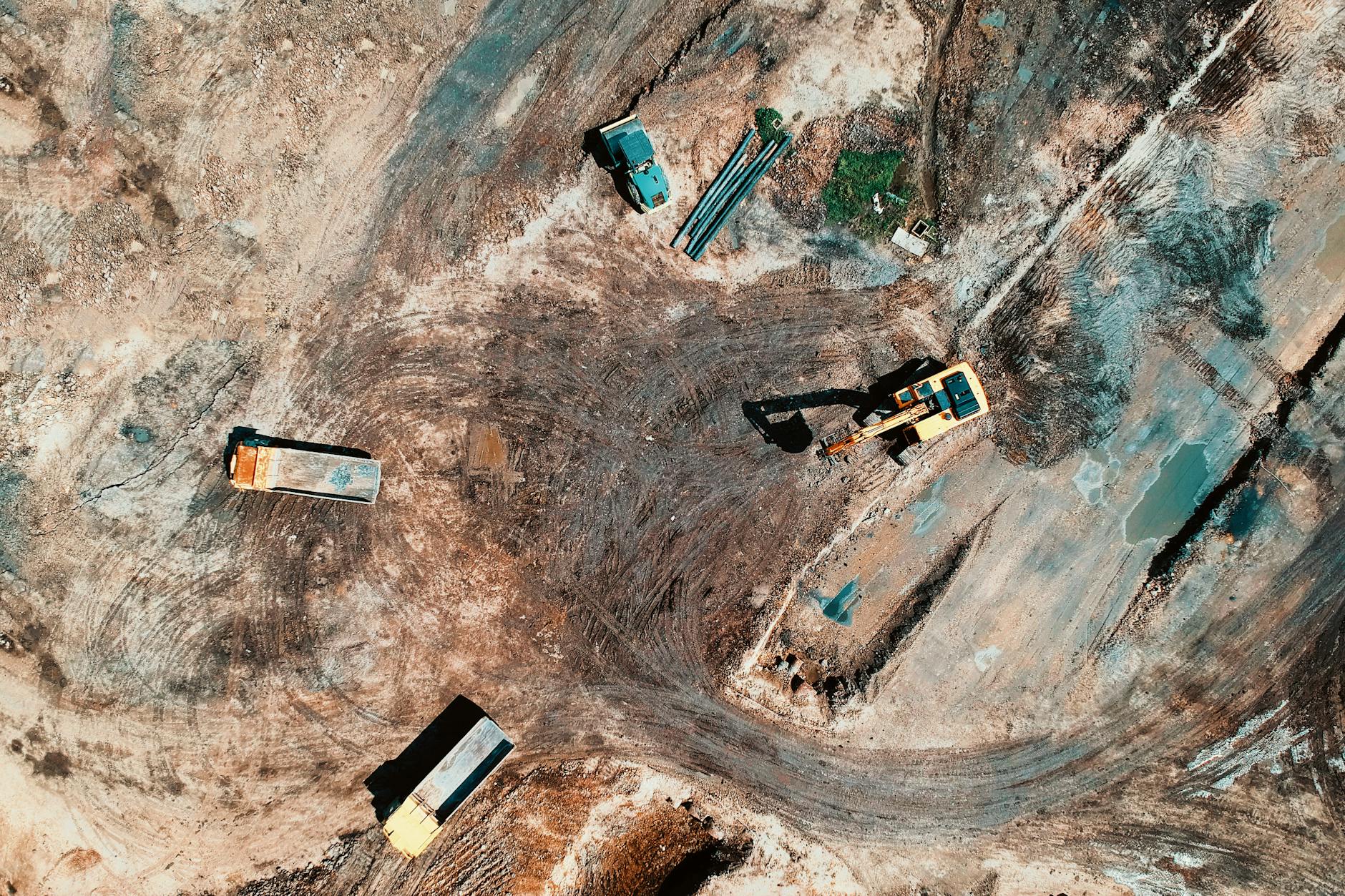 High-angle aerial view of construction site with earthmoving equipment and trucks.