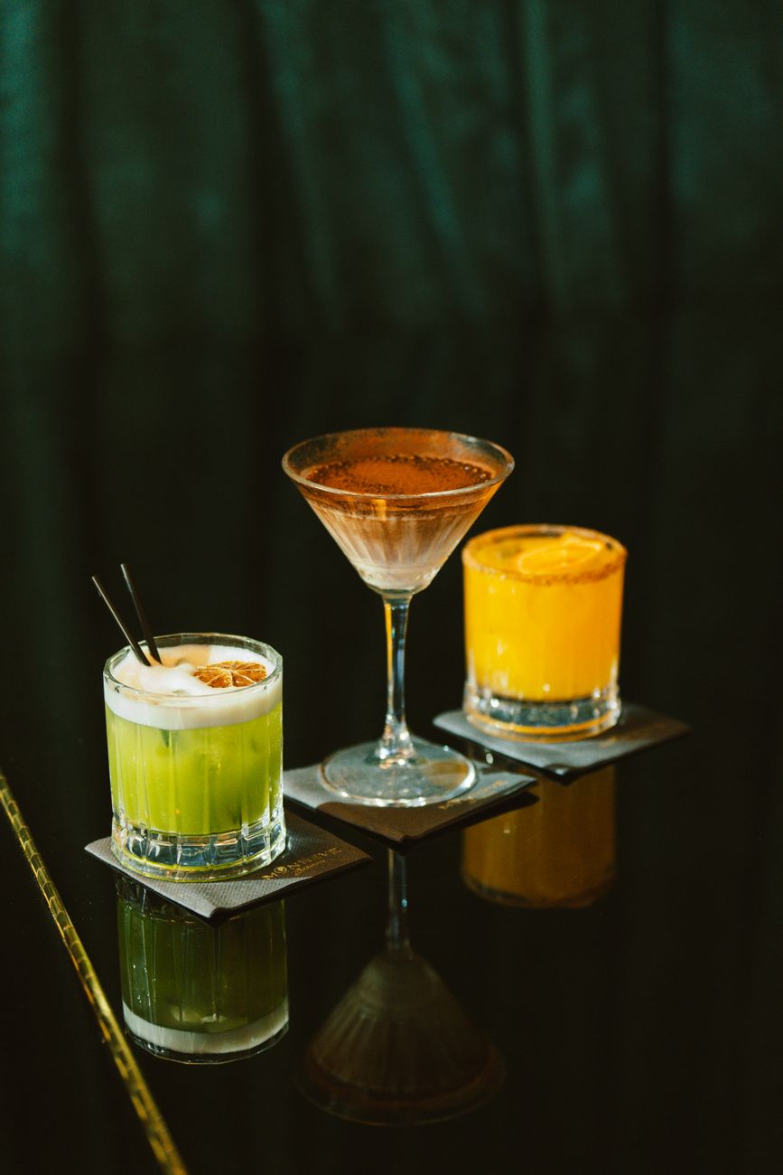Three vibrant cocktails on a reflective black table, each garnished uniquely.