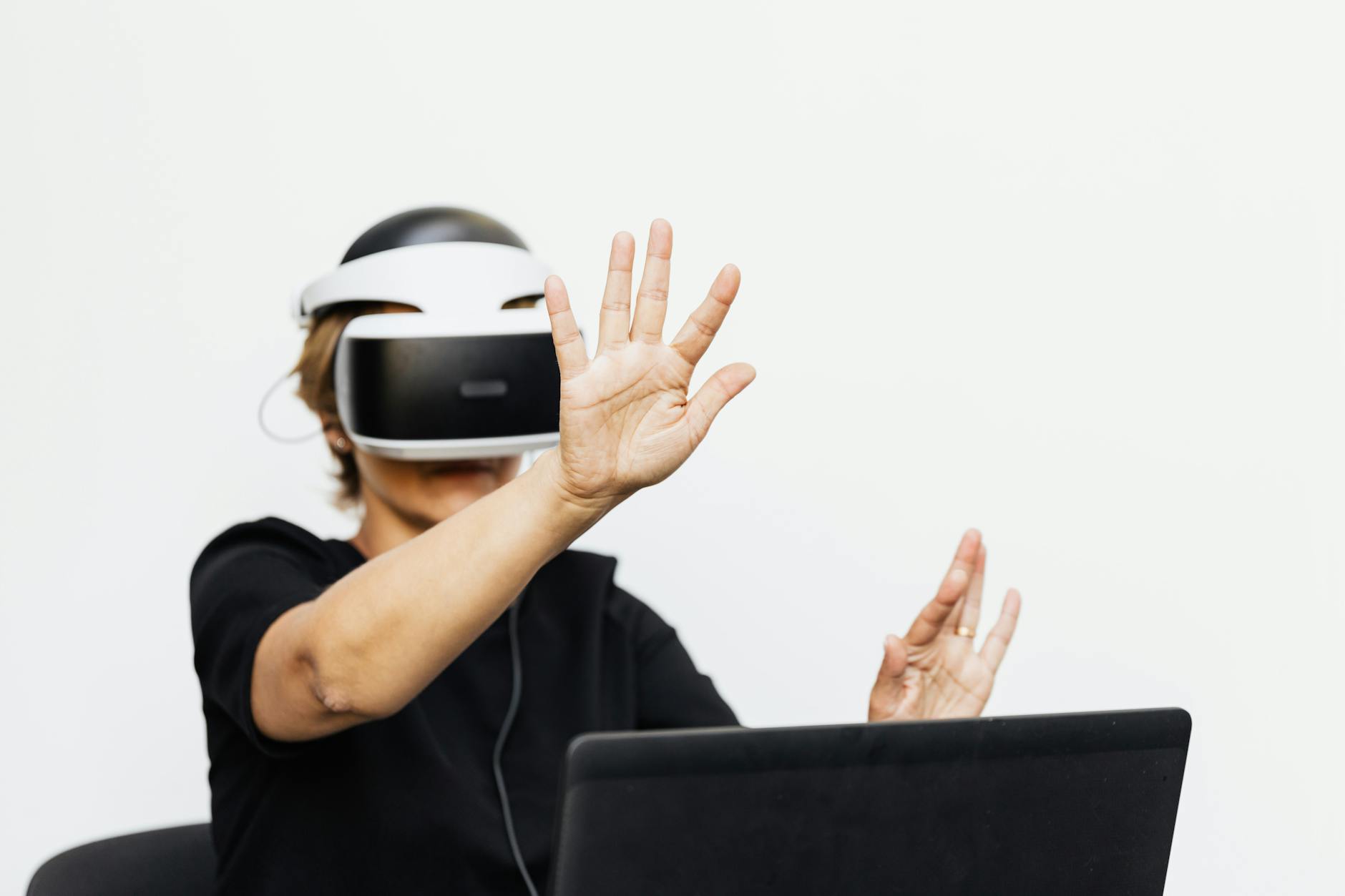 An adult wearing a VR headset interacting virtually, seated with a laptop.