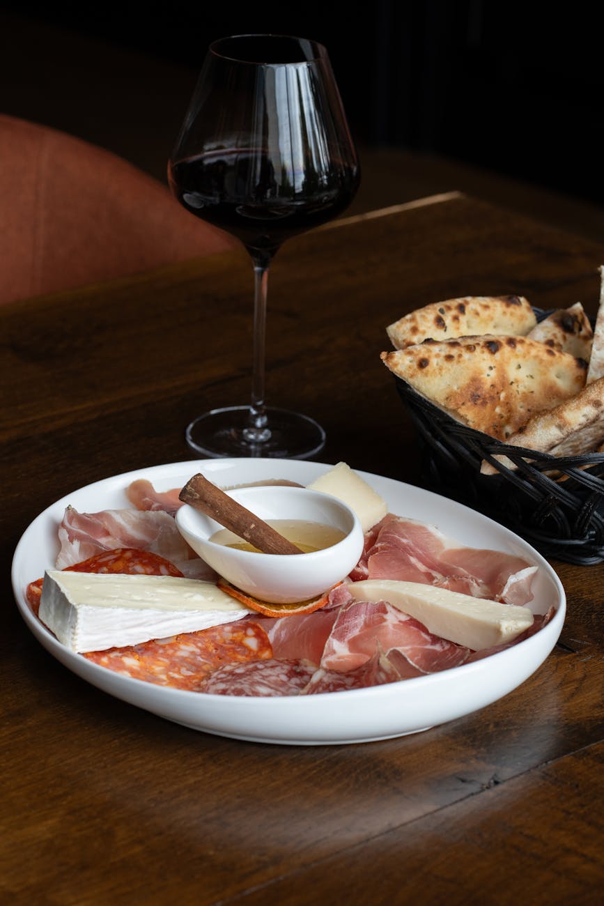 Gourmet charcuterie platter with cheese, meats, and red wine on a wooden table.
