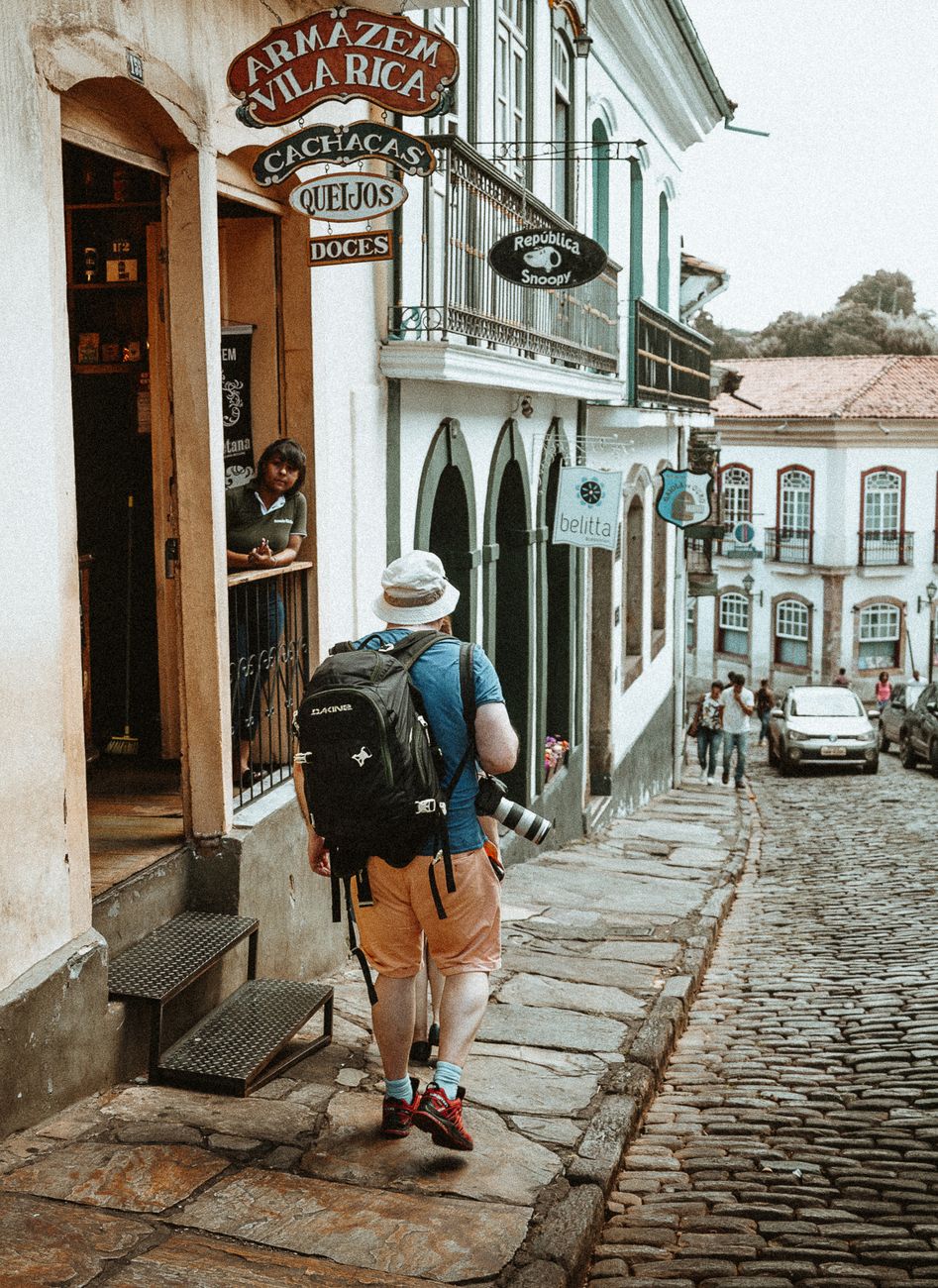 A solo traveler with a backpack walks down a cobblestone street with historic architecture in view.