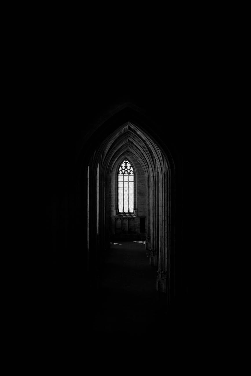 A captivating gothic archway leading to a faintly lit window, creating an eerie and mysterious atmosphere.