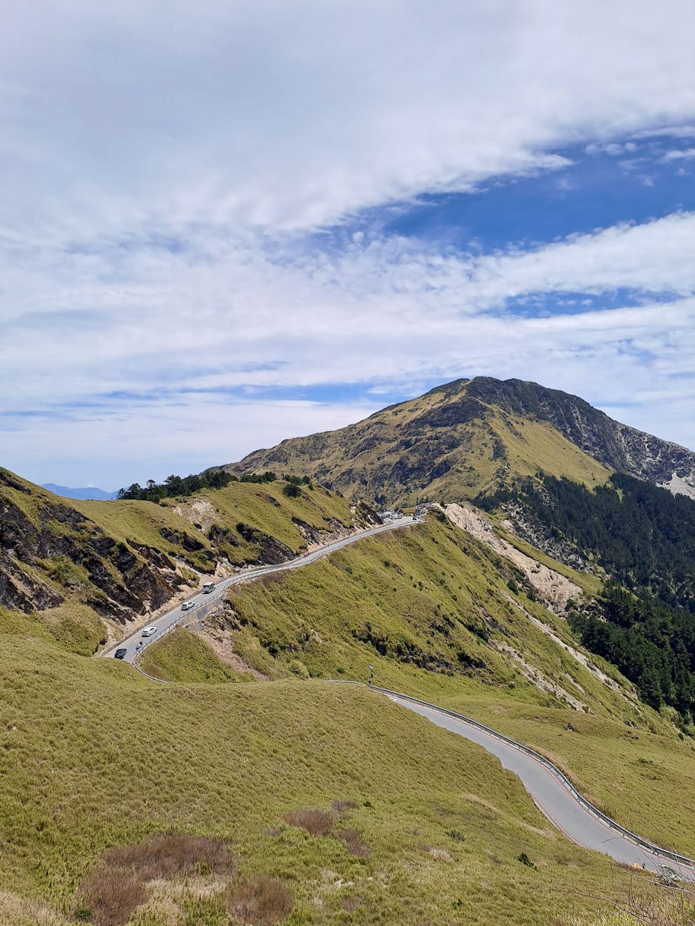 Curving road through lush green mountains under blue skies, ideal for travel and nature themes.