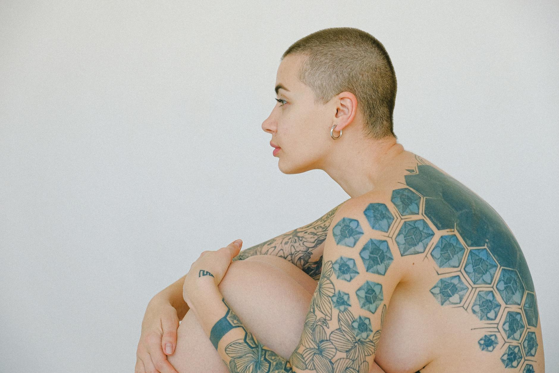 Side profile of a tattooed person with a shaved head, showcasing geometric and floral designs.