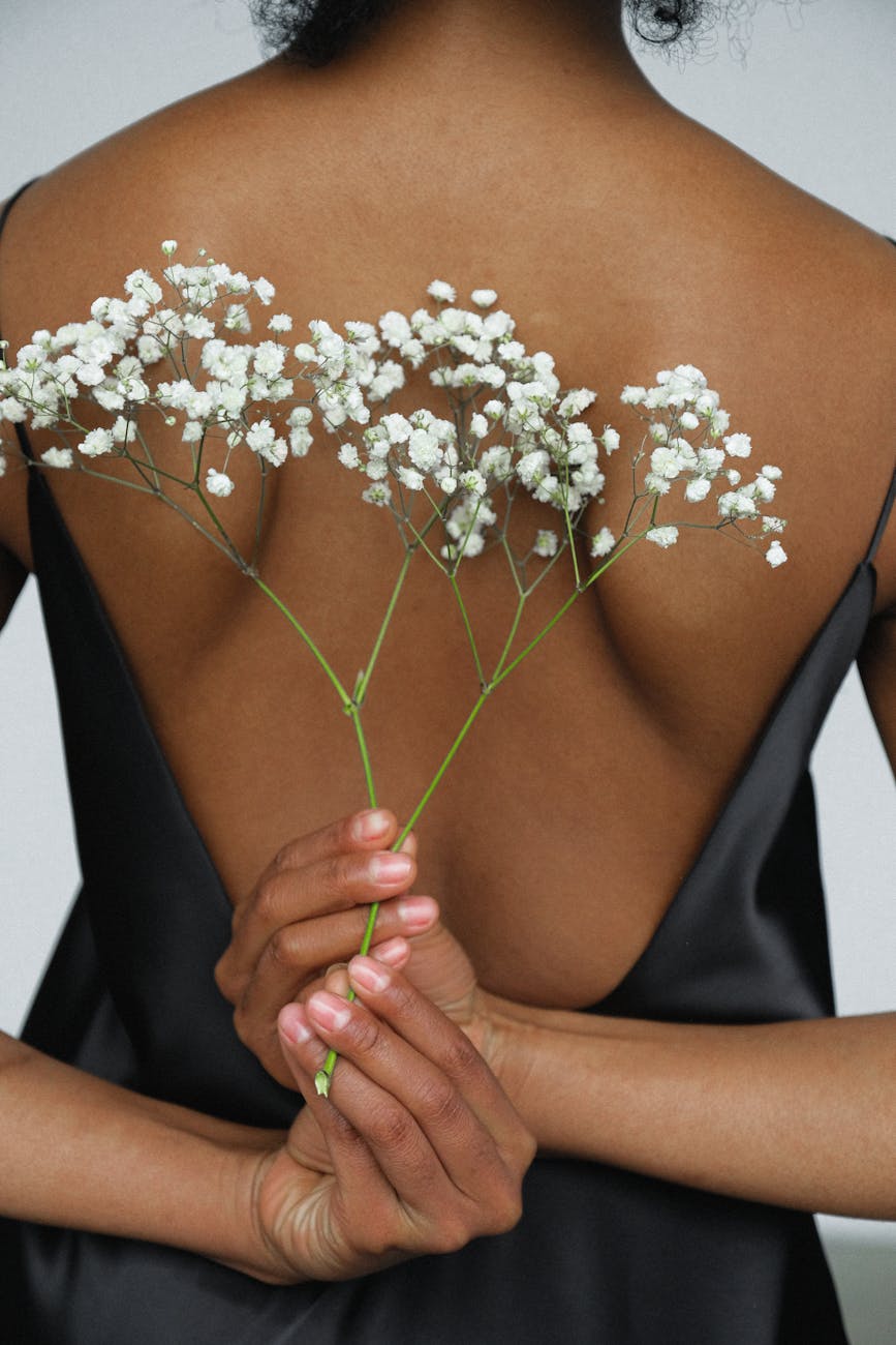 Aesthetic back view of a woman holding white flowers against an elegant black dress.