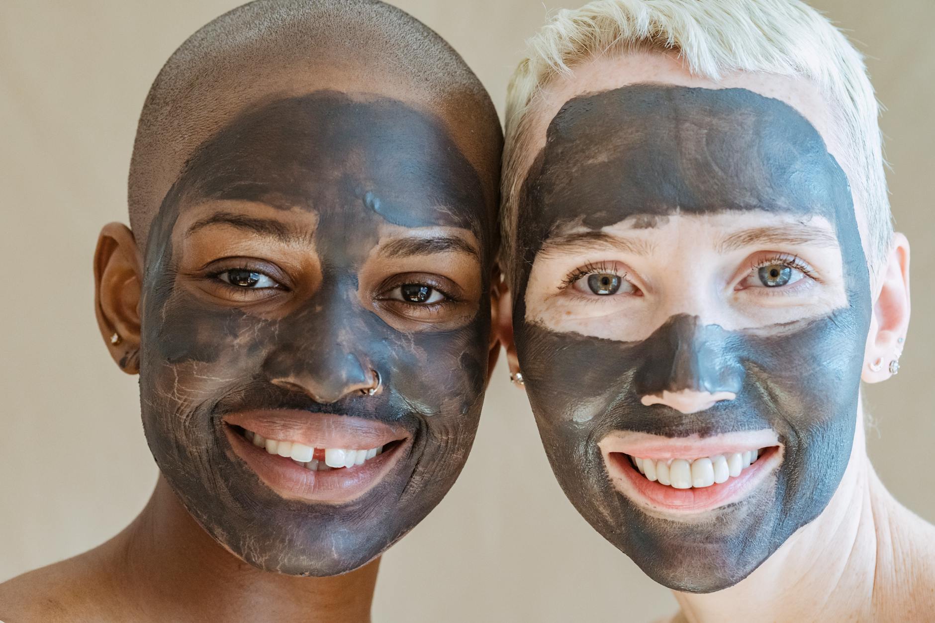 Crop young multiracial female friends with applied face masks smiling and looking at camera on beige background