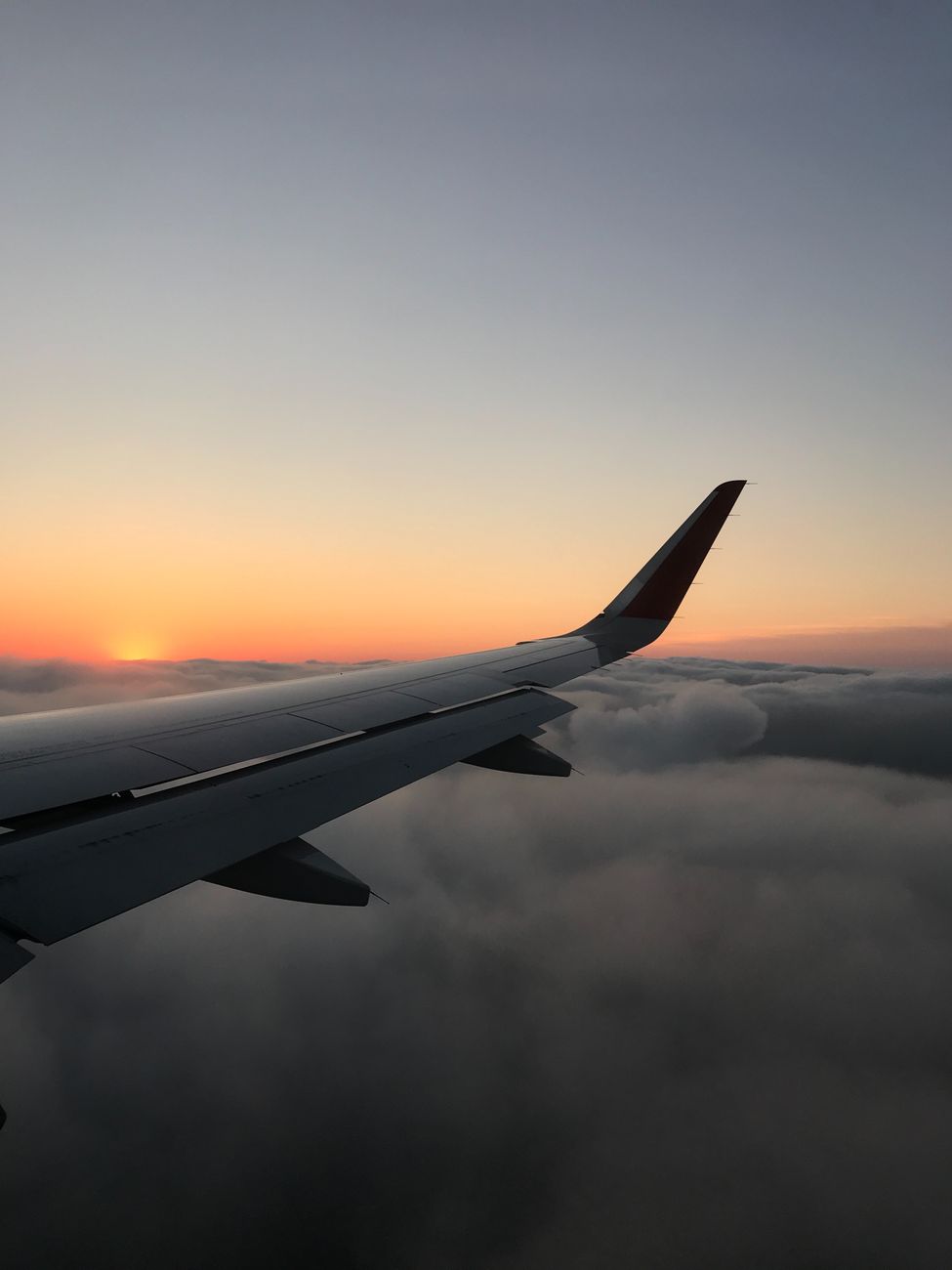 Scenic view from airplane wing at sunset, flying over clouds in serene atmosphere.