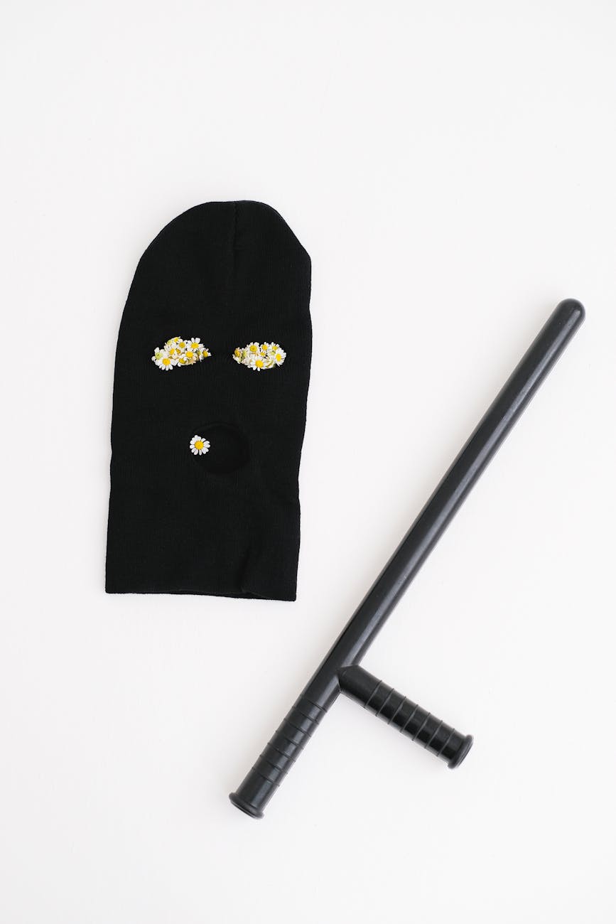 Flat lay of a black mask with a security baton on a white background.
