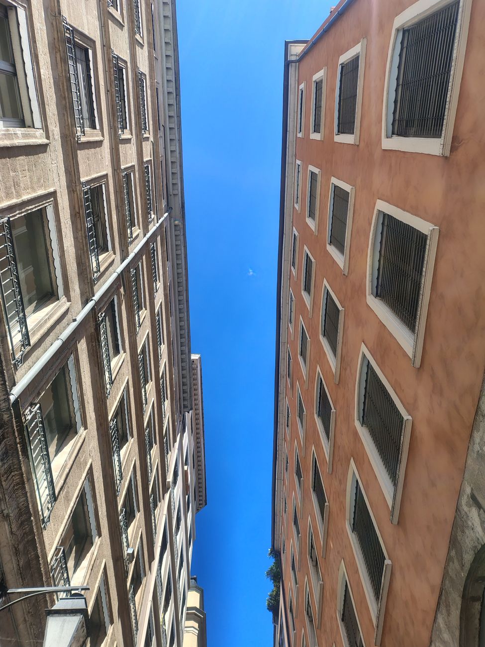 Upward view of a narrow street framed by classic European stone buildings against a clear blue sky.