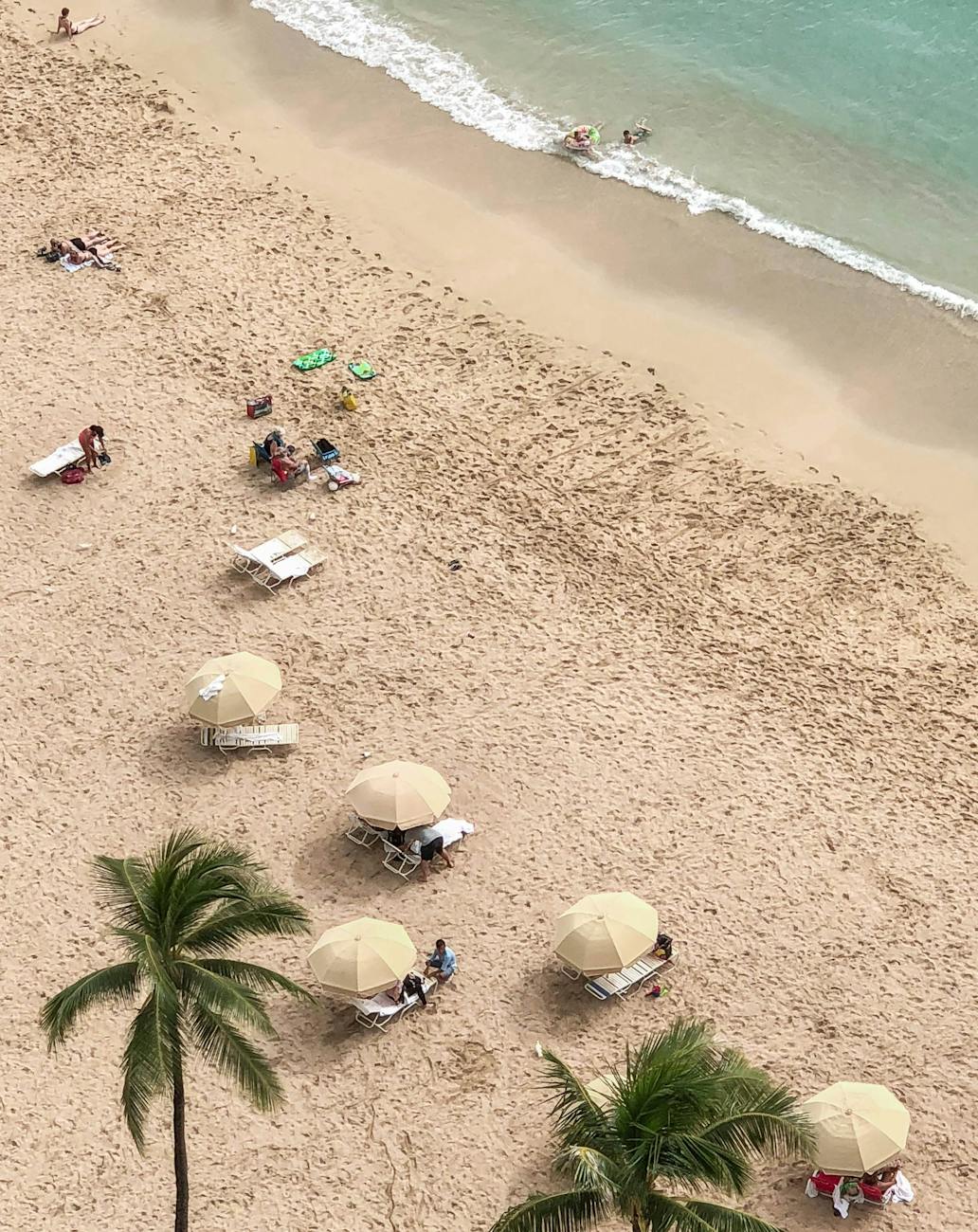 Aerial shot of a sandy tropical beach with umbrellas and people relaxing near the ocean.