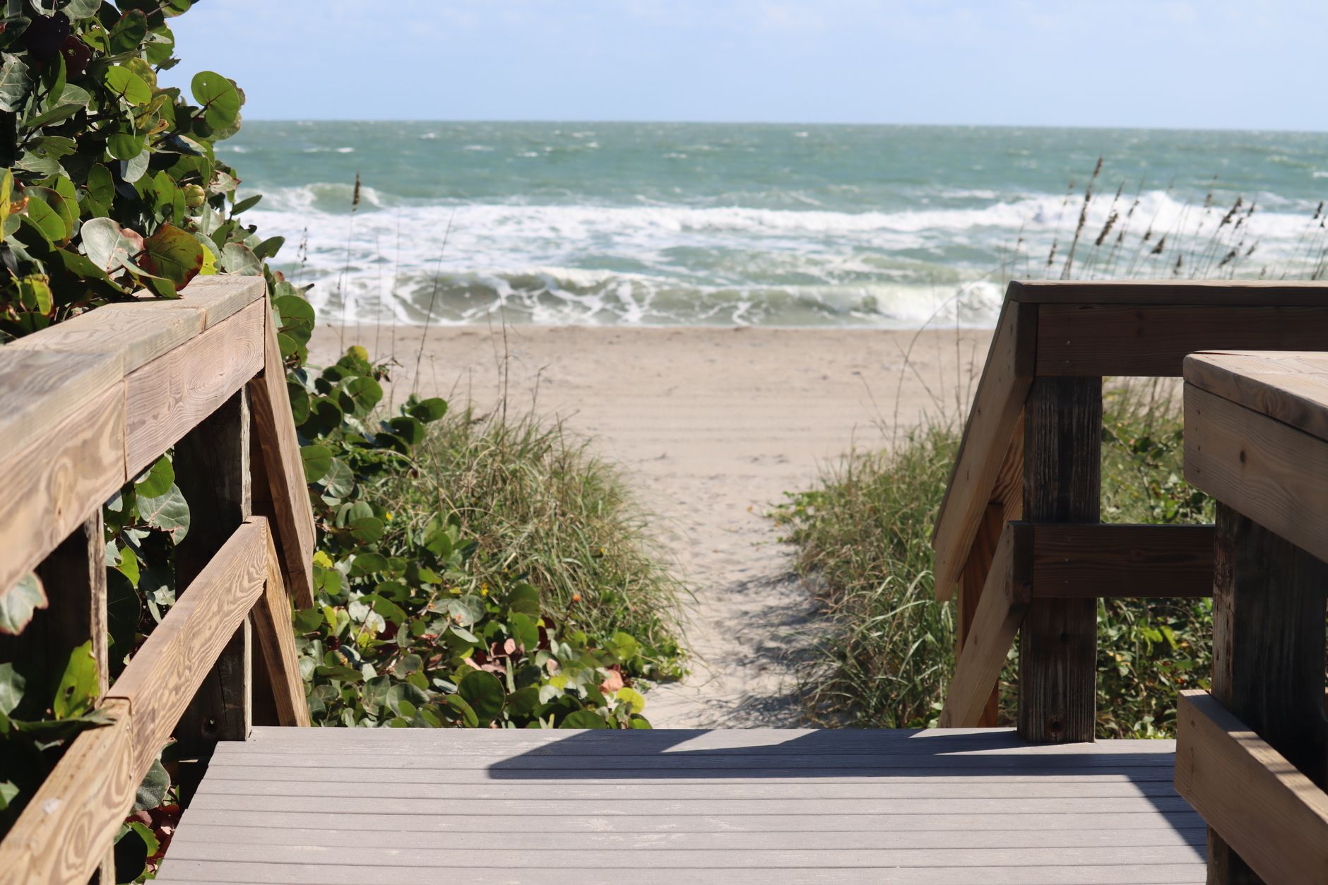 Wooden boardwalk leading to a sandy beach with waves in the background.