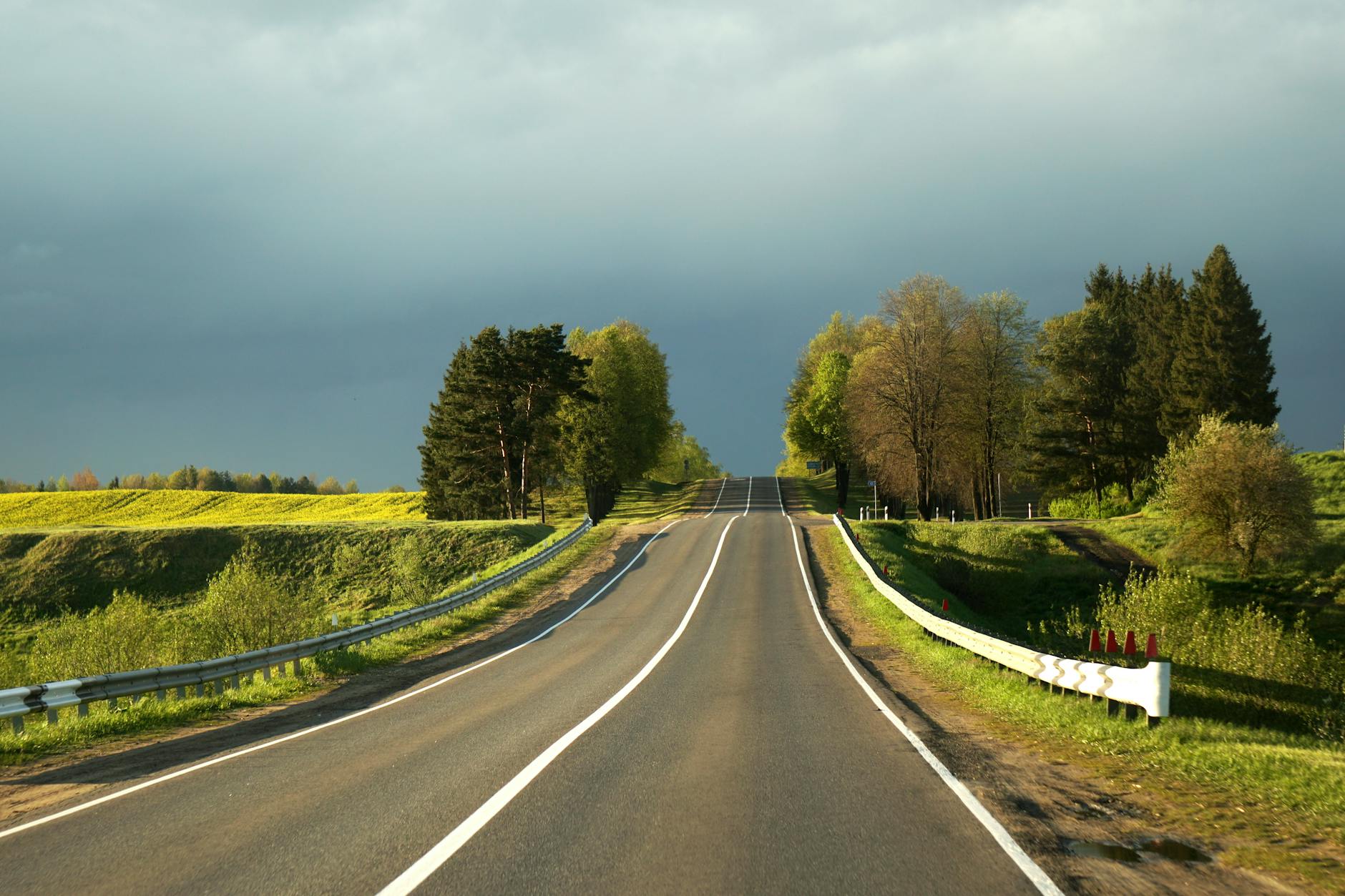 Empty country road winding through lush greenery under a cloudy sky, perfect for travel inspiration.